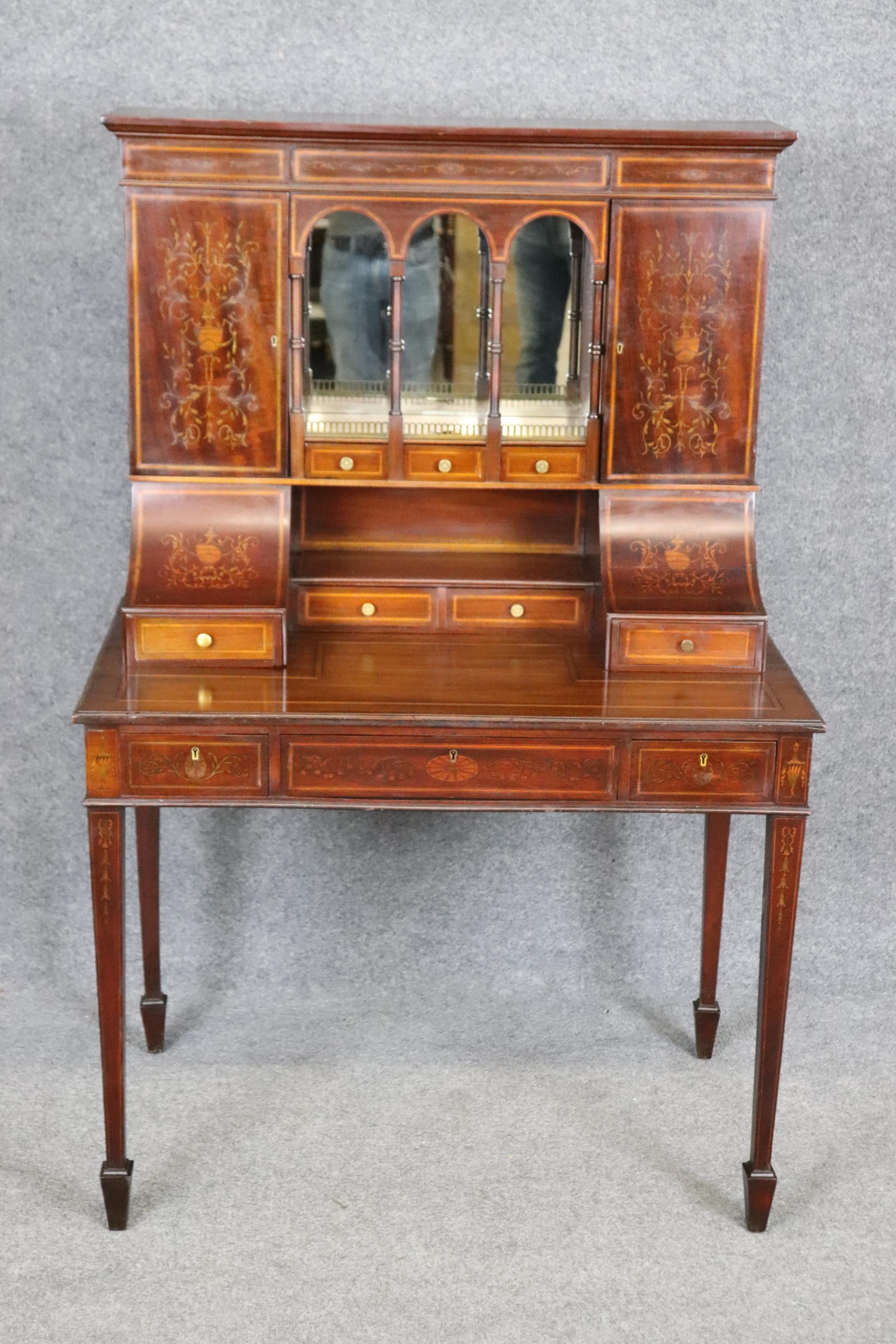 Il s'agit d'une forme très rare de bureau. Le bureau est incrusté dans la tradition de Carlton House et présente des placages teintés et un fond en acajou foncé avec un dos en miroir derrière des fuseaux. Le bureau est en deux parties et est