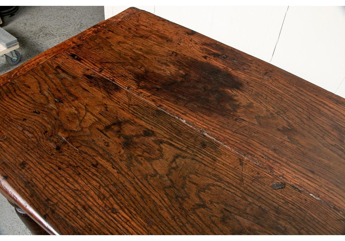 Une très belle table de taverne recréée en bois ancien. Avec un dessus de planche à pain à deux panneaux en surplomb. La table a un tablier sculpté sur tous les côtés avec des éléments façonnés. Monté sur de lourds pieds carrés et tournés avec une