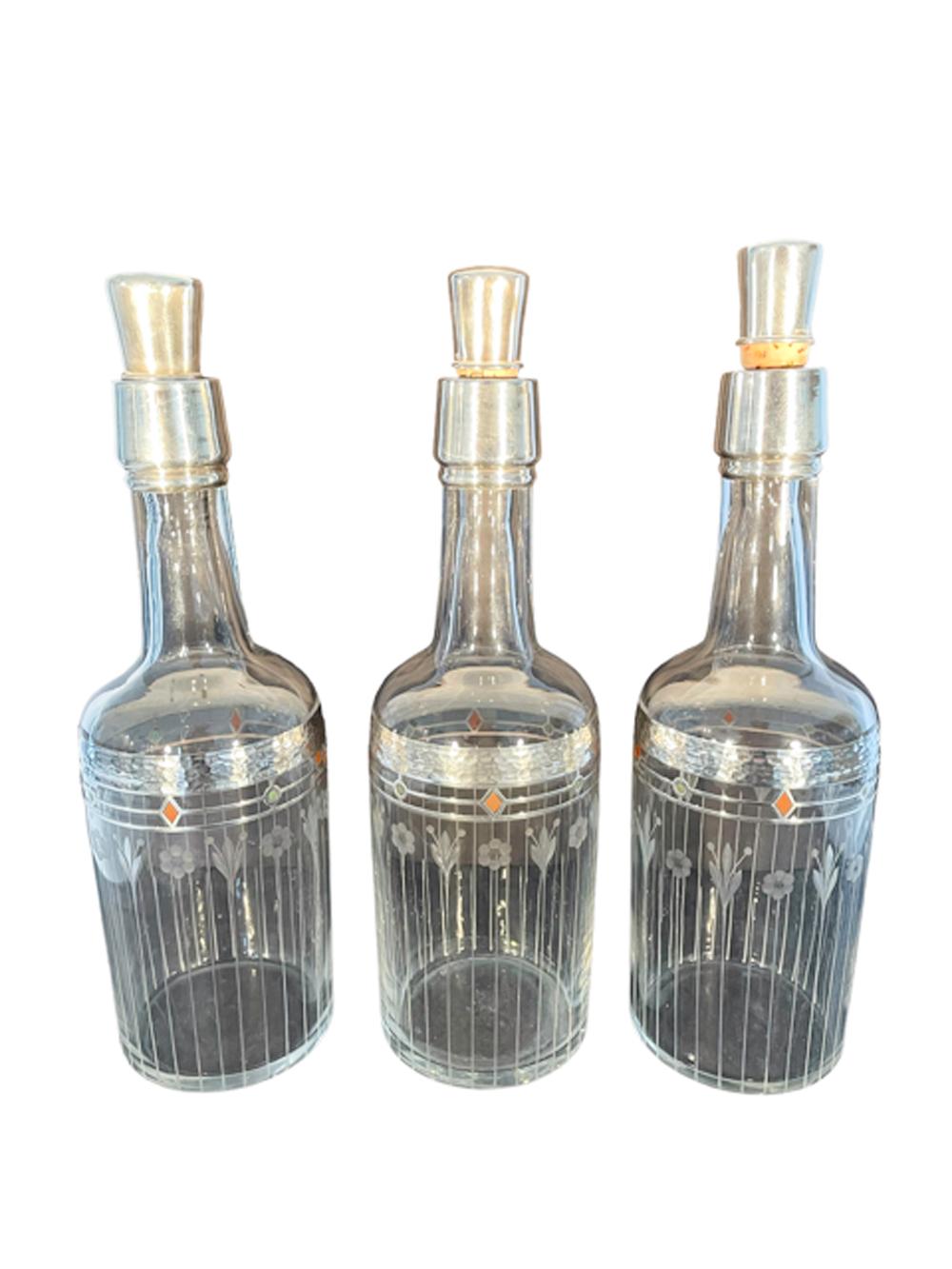 Rare set of three matched Art Deco back bar bottles or decanters of clear glass, in the manner of T.G. Hawkes & Co. Each with a silver covered cork stopper and silver overlay at the top of the neck and with a band of hand hammered silver at the