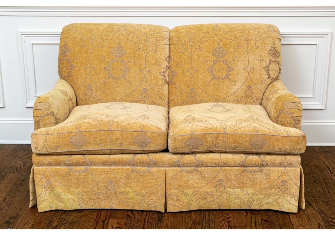 Comfortable two-seat settee with scrolled back and arms. With deep tailored skirt pleated at the corners. Upholstered in a custom gold tone patterned cut Chenille type fabric with comfortable high-back cushions. 
Measures: Length 60