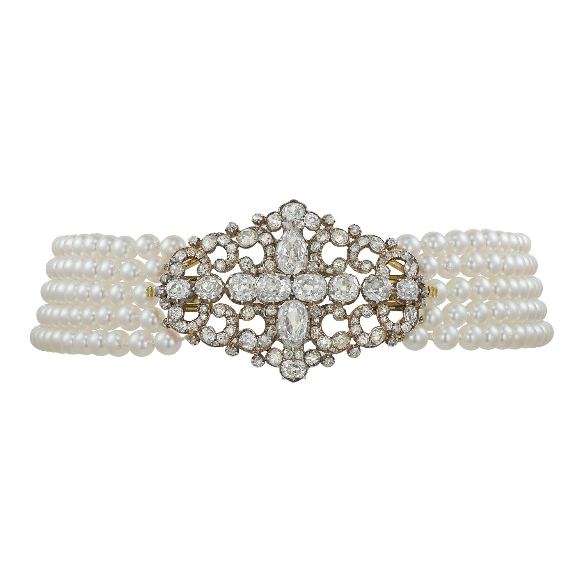 A fine Victorian diamond scroll brooch strung here as a centrepiece on a cultured pearl choker necklace, centrally-set set with a row of graduating old European-cut diamonds and two old pear-shape-cut diamonds set vertically, all within an openwork