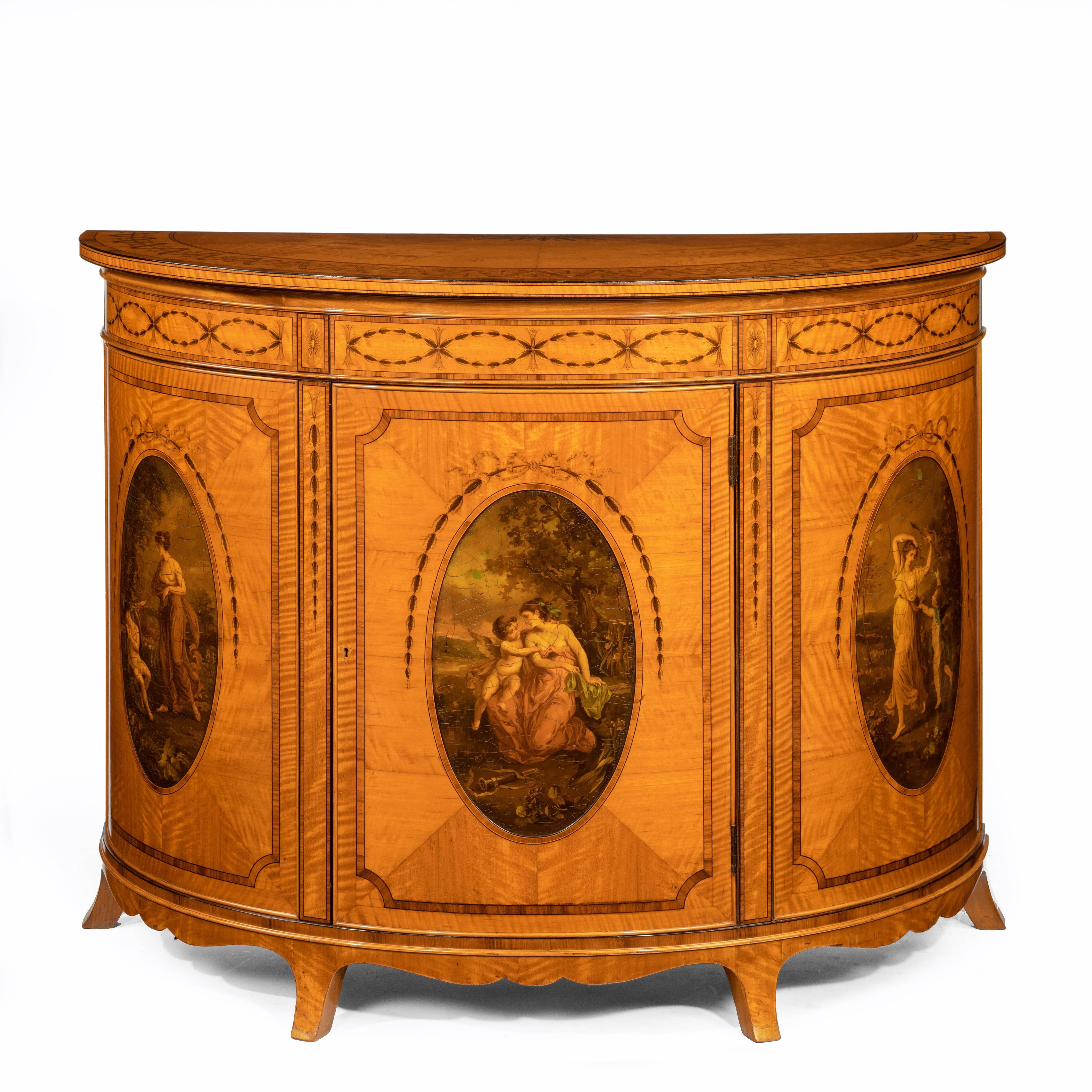 A fine Victorian Sheraton revival West Indian satinwood demi lune commode, the semi-circular top above three panels, the central one disguising a cupboard door, painted with three ovals in the style of Angelica Kaufman with classical scenes of Venus