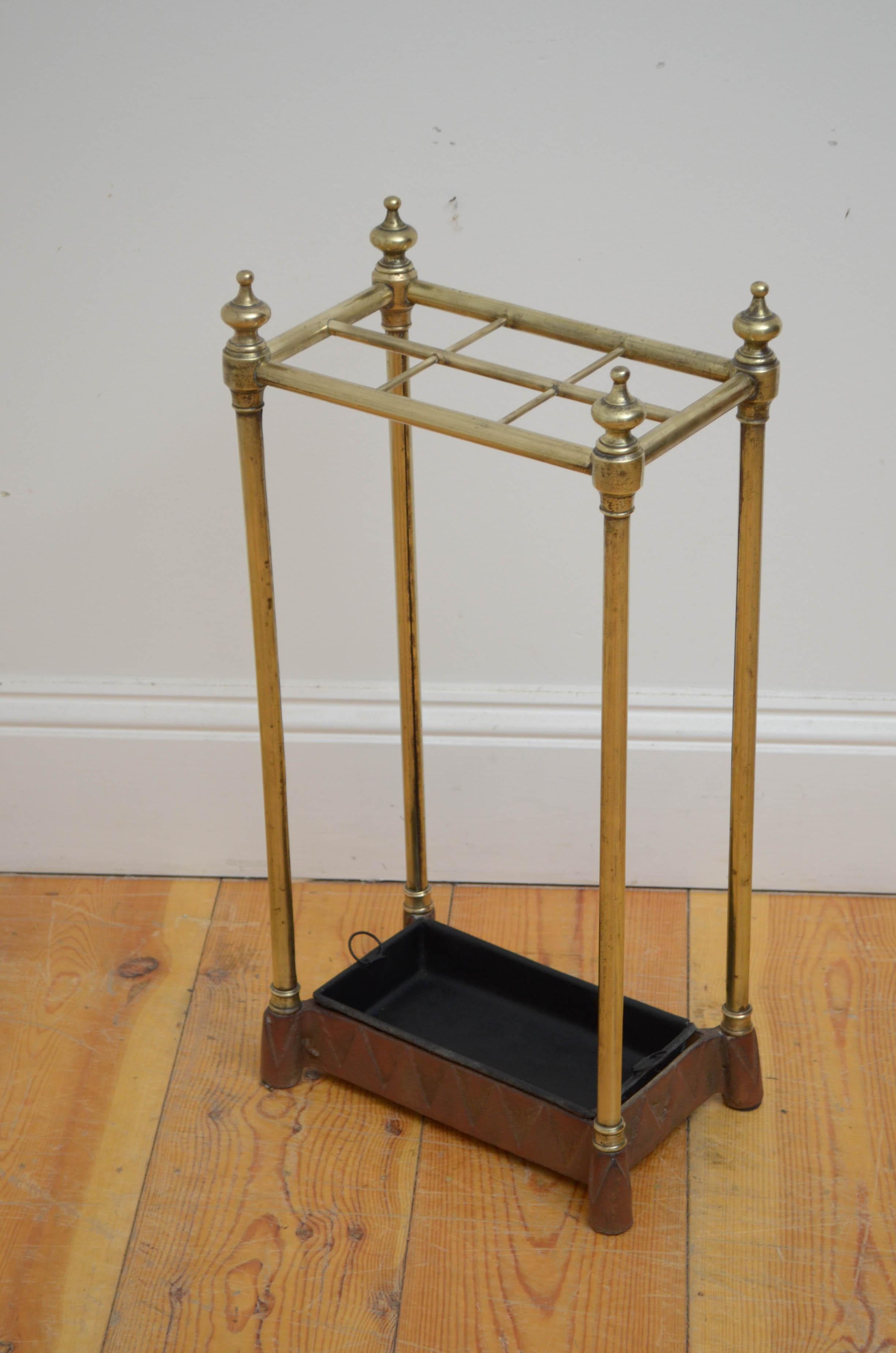 0569 English Victorian brass umbrella stand, having six divisions flanked by decorative finials removable drip tray and cast iron base with dog tooth decoration and original oxide paint. This antique umbrella stand has been sympathetically polished