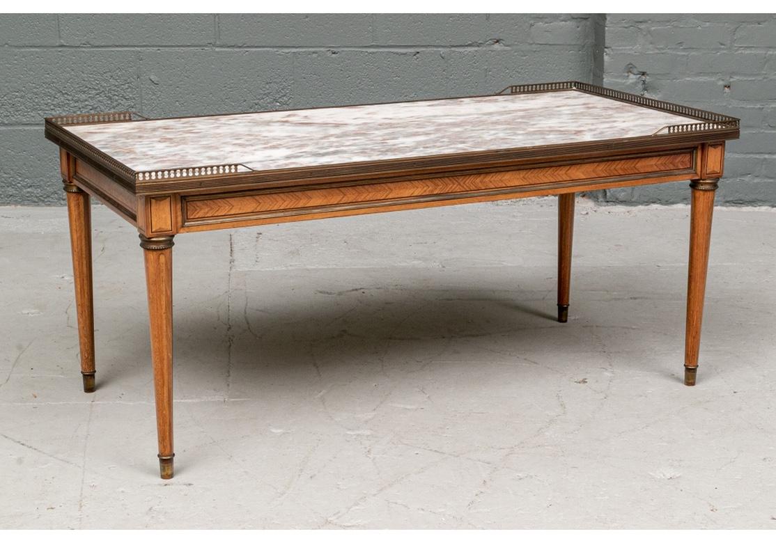 A rectangular low table in walnut with a parquetry herringbone decorated apron panel with brass banding. The tapering cylindrical legs with inlaid faux flutes and brass collars. Brass peg feet. The fine pink and white marble top with brass 3/4