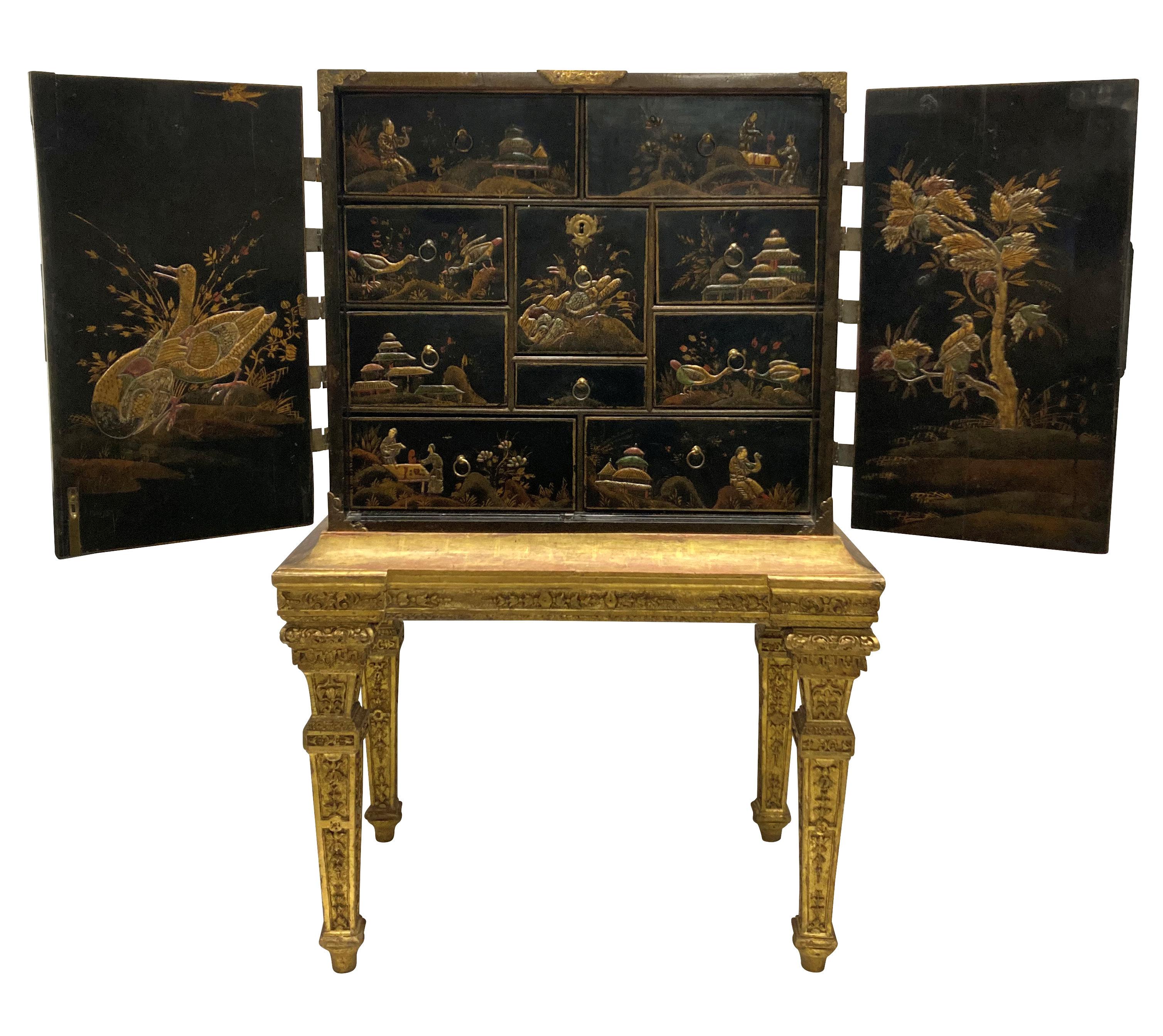 A William and Mary Gilt-Japanned Chinoiserie cabinet on gilt wood stand. The cabinet depicting Court and rural scenes, with pierced and engraved strapwork mounts and elaborate escutcheon plate with original lock and key. The interior fitted with ten