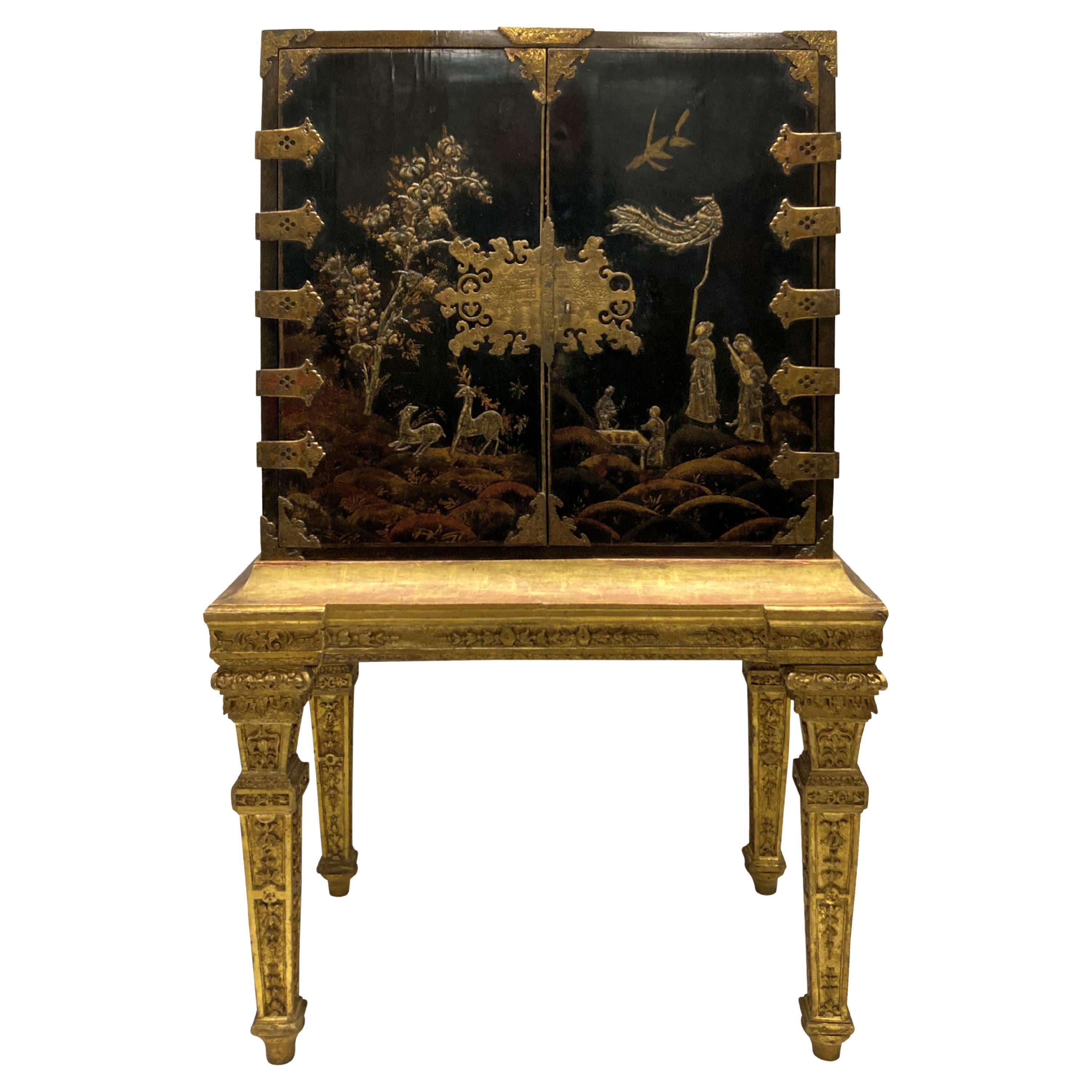 Mueble de chinoiserie dorada de William & Mary sobre peana de madera dorada. El mueble representa escenas cortesanas y campestres, con monturas caladas y grabadas a cincel y una elaborada placa con escudo, con cerradura y llave originales. El
