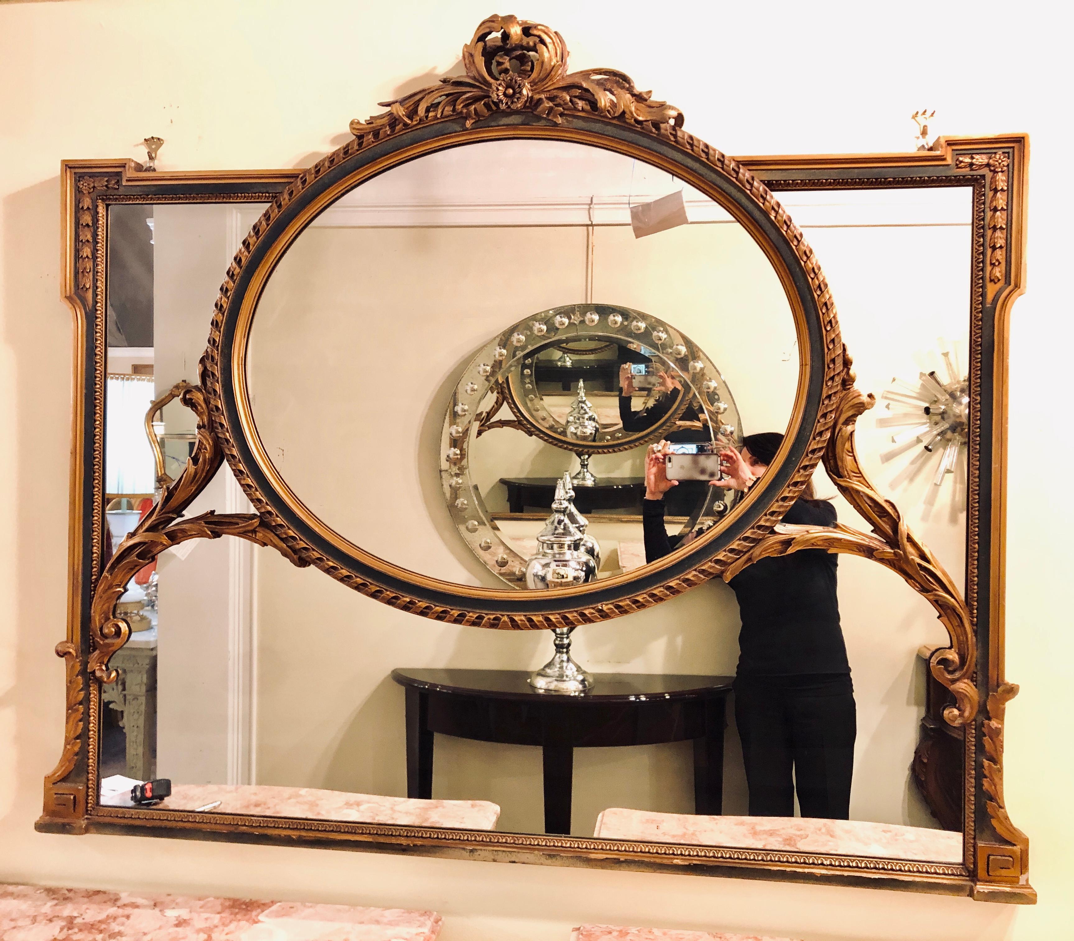 A finely carved Hollywood Regency or Adams style over the mantel (fireplace) or wall mirror. This stunning and one of a kind over the mantel (fireplace) or wall / console mirror is simply magnificent. The gilt wooden and greenish paint decorated