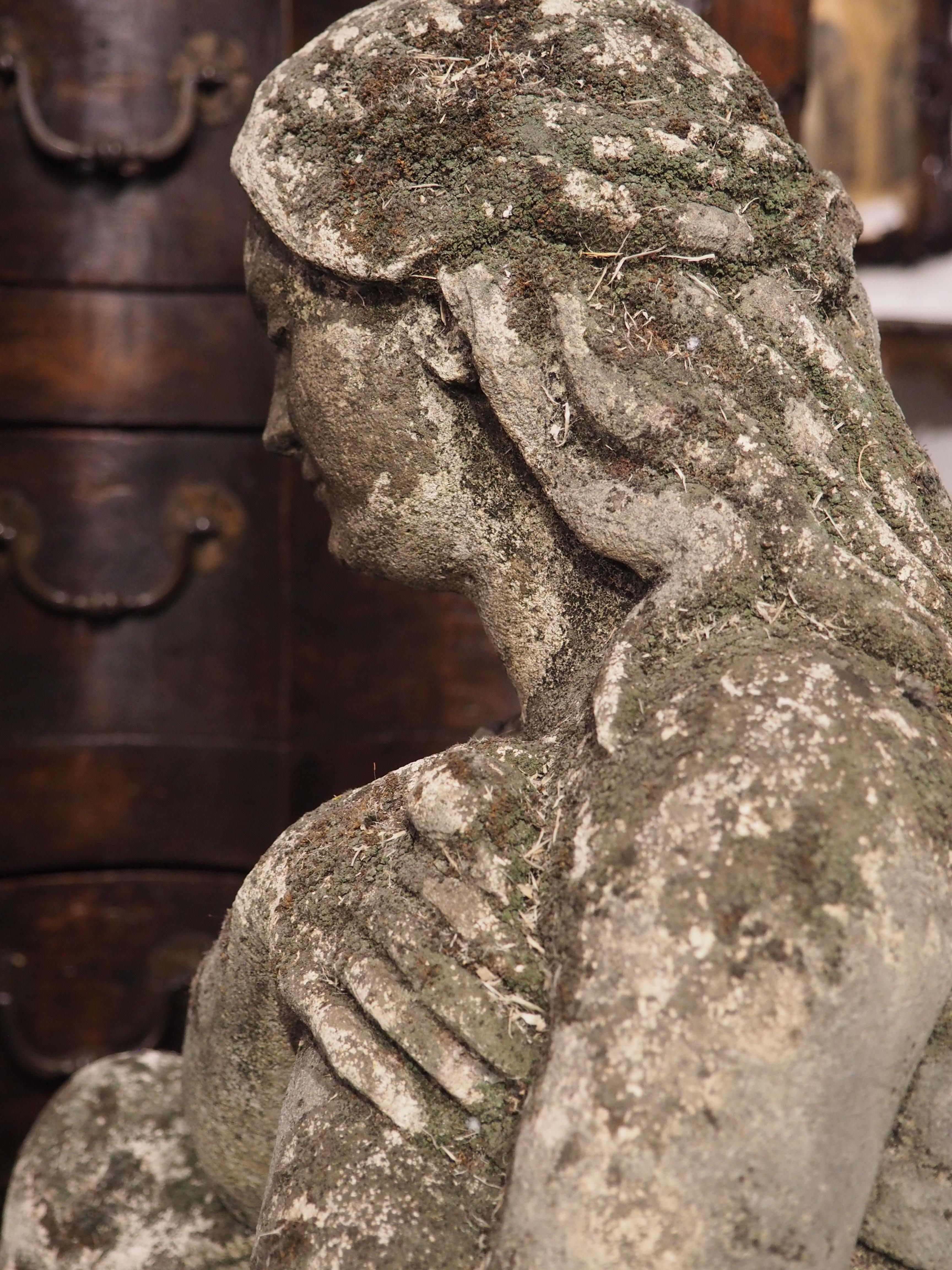 Cette statue finement sculptée représente une femme tenant un oiseau près de sa poitrine. Il a été sculpté à la main en Italie à partir d'un bloc de pierre. On peut voir la femme solennelle agenouillée sur son genou gauche au-dessus d'un grand socle