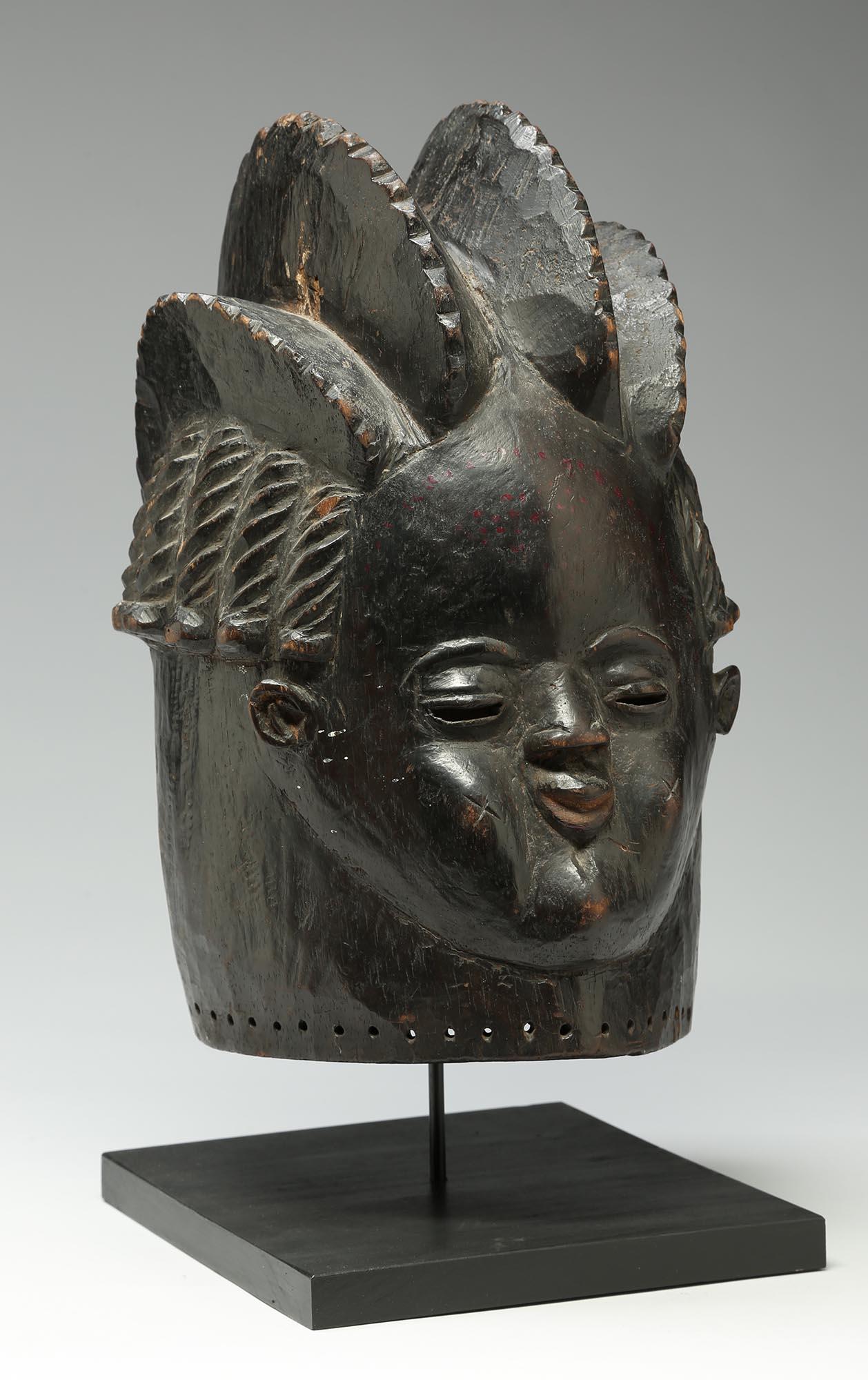 Very finely carved blackened wood helmet mask from the Bassa people in Liberia. Early 20th century with great crested hairstyle with rows of braids on side of head and welcoming face. On custom wood and metal stand, mask 14 3/4 inches high, on base