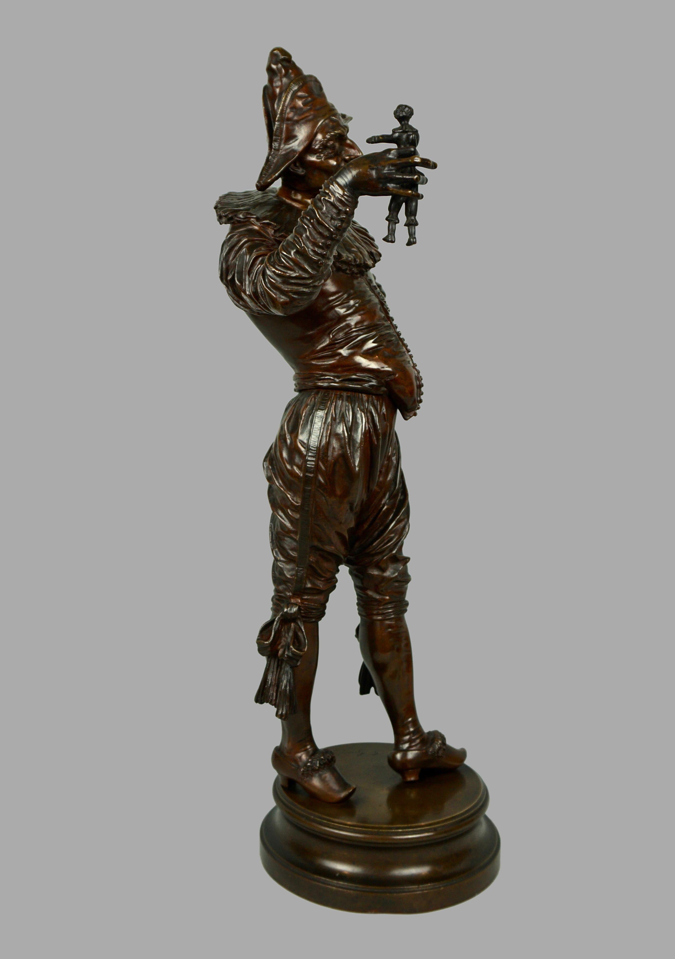 An exceptionally well-cast bronze sculpture with brown patina depicting a harlequin holding a doll, the elaborately dressed figure with an expressive face and imposing posture resting on a bronze circular base signed 