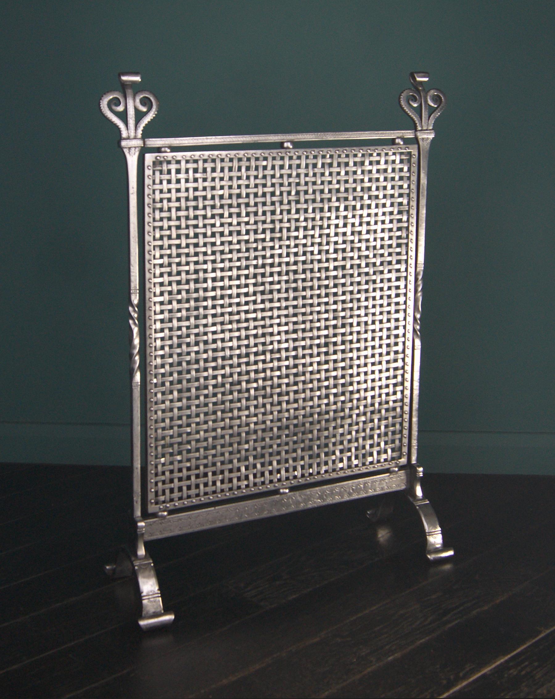 A finely engraved early 20th century polished wrought fire screen by C Downer, Campden, Glos.  The fire screen with densely latticed mesh riveted to inner frame, extensive intricate engraving to surrounding structure and beautifully scrolled finials