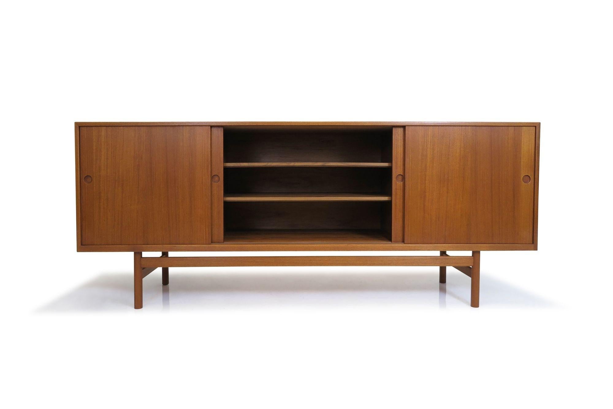 Mid-century teak credenza attributed to Hans J. Wegner, Denmark, 1955. The sideboard is handcrafted from old-growth teak with mitered corners and features four sliding cabinet doors with recessed round pulls. The doors open to reveal a teak interior
