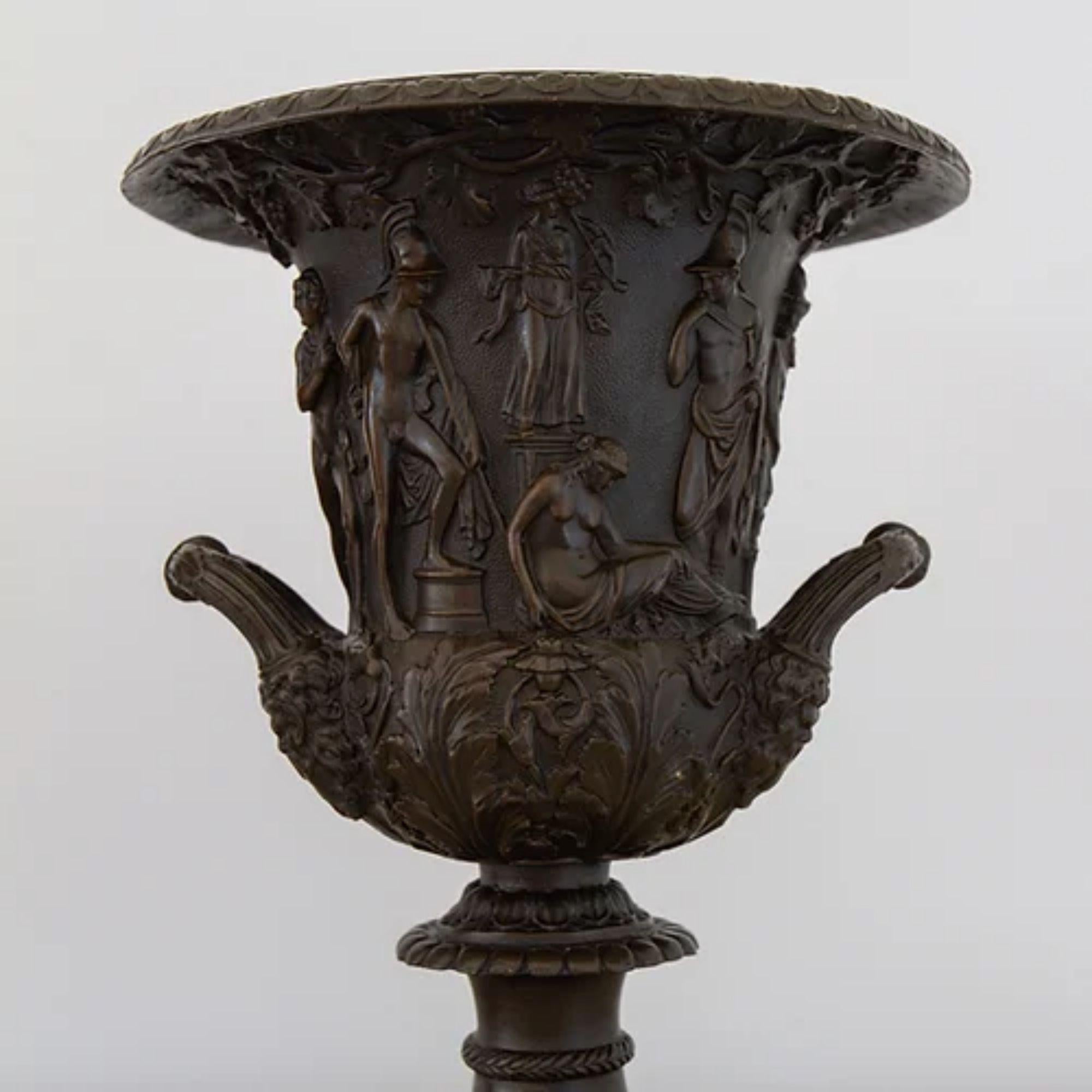 A pair of 19th century Grand Tour bronze urns, finely carved with neoclassical depictions, potentially showing the Roman conquering of Greece. The base of the campana vase has intricate acanthus leaf carvings attached to two handles, and the rim is