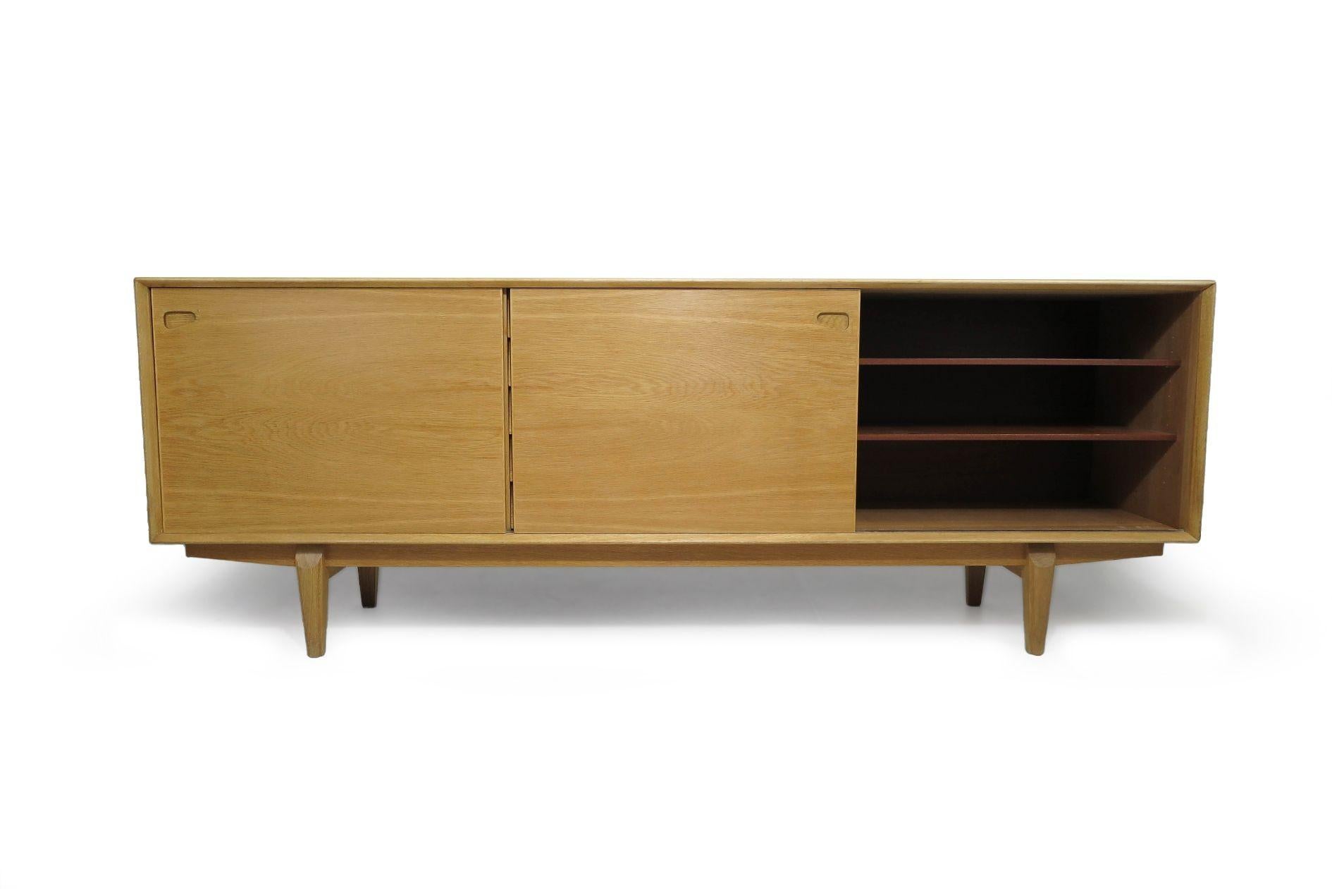 This impressive Danish credenza is expertly handcrafted from white oak, featuring fine joinery with mitered beveled edges, five center drawers, and sliding doors on either side, each with carved recessed pulls. The doors open to reveal an interior