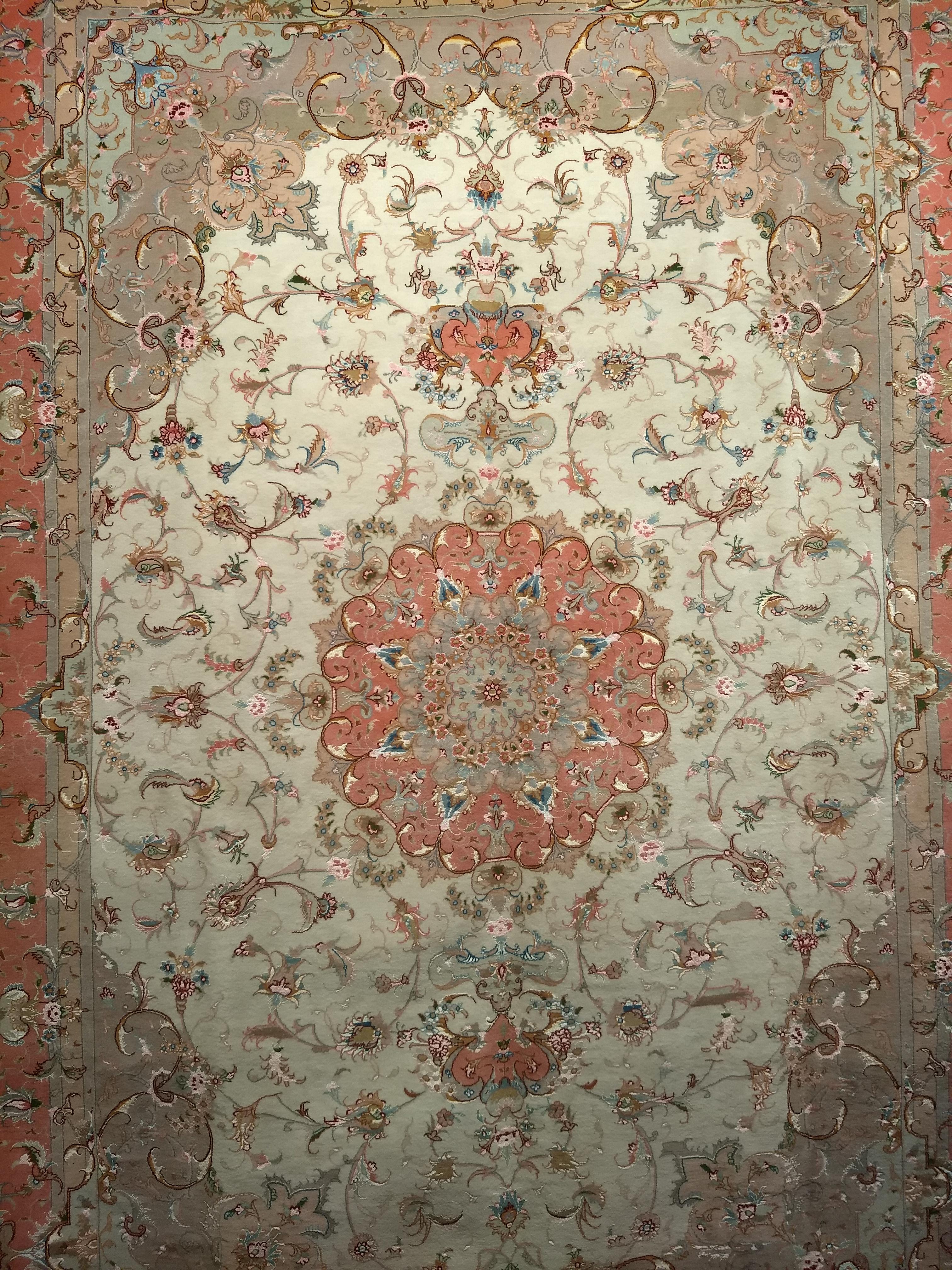 A beautiful Persian Tabriz room size rug in a classic floral pattern in ivory, salmon, camel and green from the late 1900s.  The Tabriz from a fine workshop has a central medallion in a floral pattern in salmon, green, blue, and red colors.   The