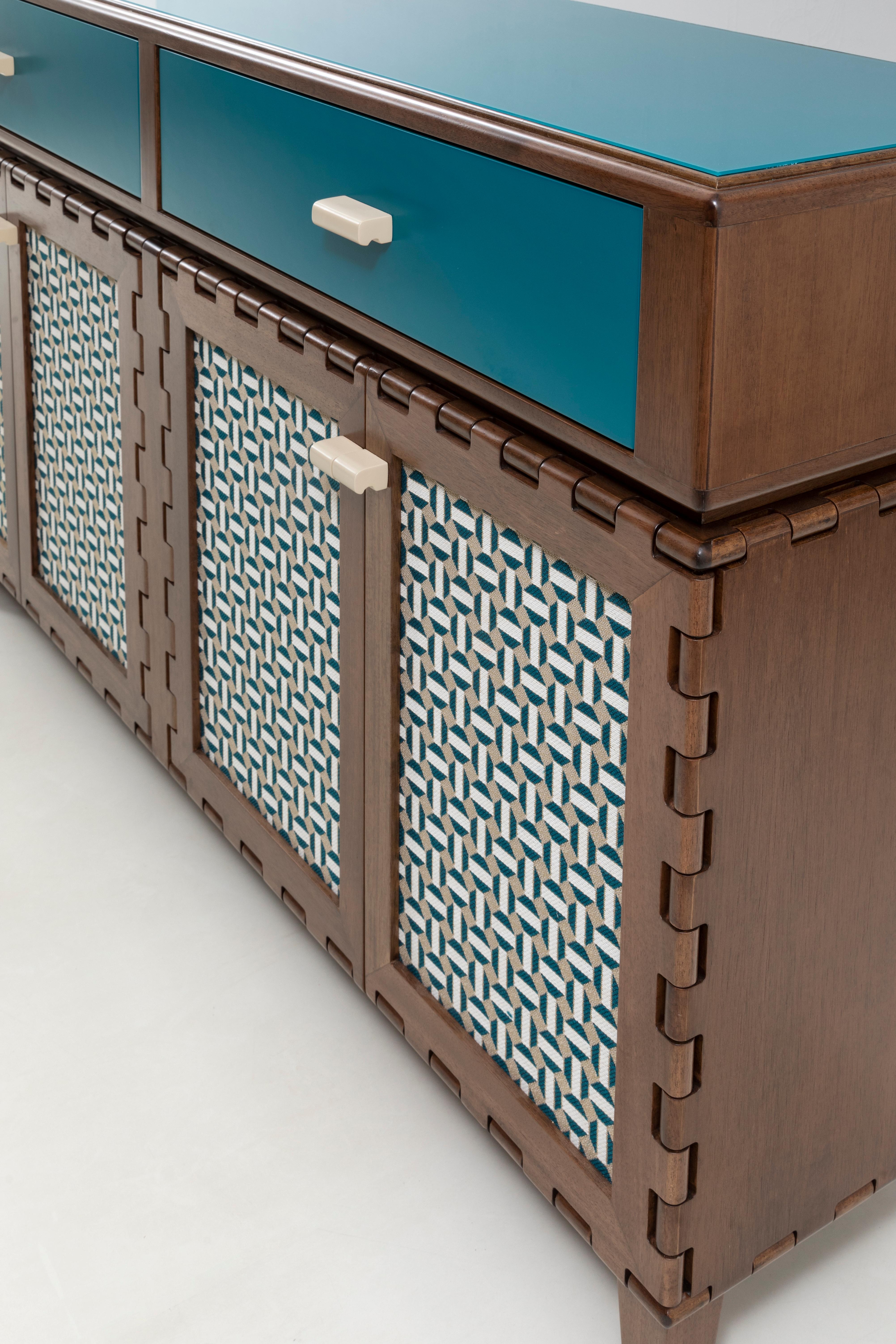 Handcrafted sideboard cabinet in wood and lacquer with fabric inserts and blue glass top. The wood and lacquer color highlights the simplicity of the design details and framed the richness of the fabric's pattern. The modular quality of the