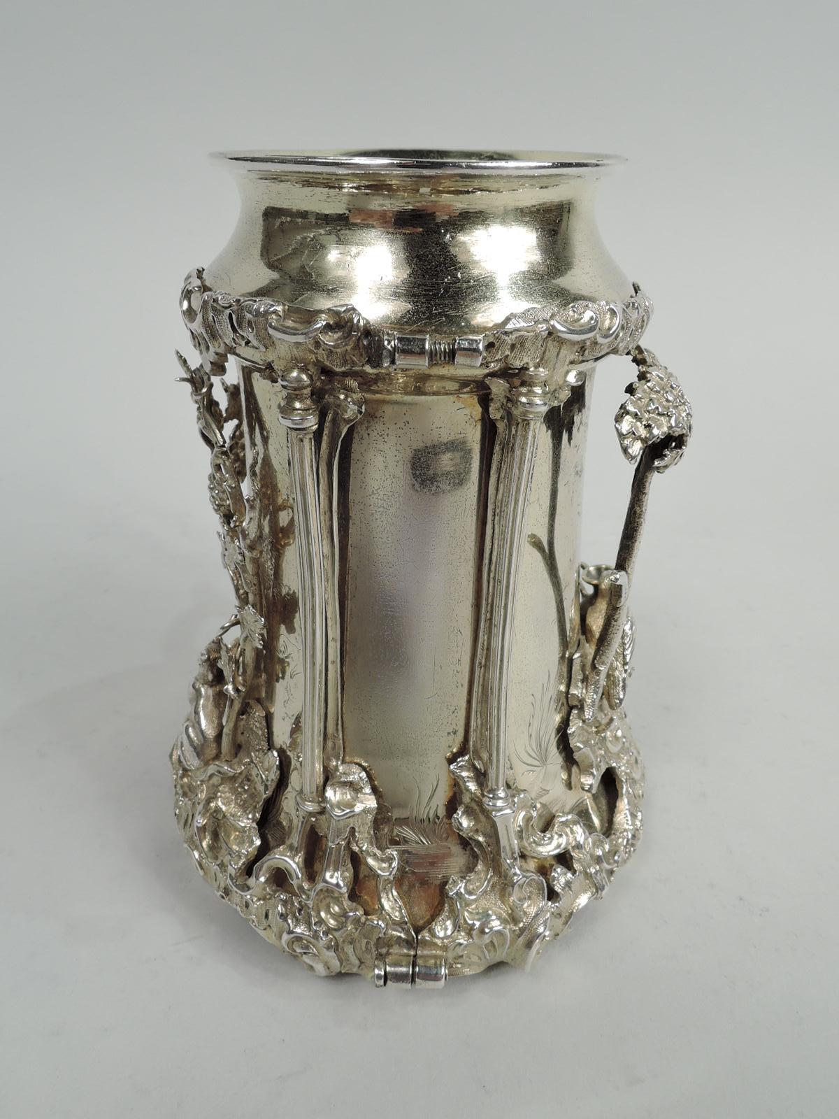 Victorian gilt sterling silver christening mug. Made Joseph Angell in London in 1860. Cylindrical with spread base, canted shoulder and flared mouth rim. Handle leaf-capped and -wrapped with volute-scroll terminal. Applied ornament depicting two