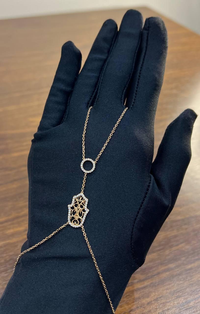 Elegantly crafted in gold, this full hand bracelet features a delicate chain design. At its center, a beautifully intricate hamsa hand motif is adorned with ornate filigree work, adding a touch of sophistication. Beautiful brilliant diamonds are