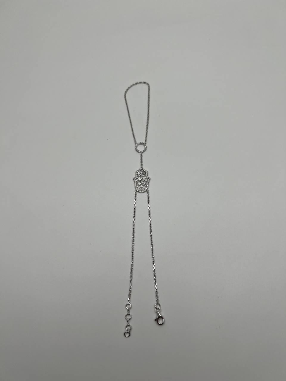 Ce bracelet exquis est composé d'une délicate chaîne en or blanc ornée d'un motif central de main Hamsa, travaillé de manière complexe avec des détails ajourés. La pièce comprend une chaîne réglable avec un fermoir en forme de homard pour un