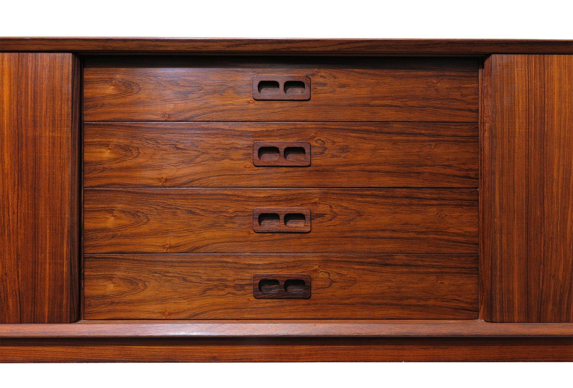 Danish Modern credenza circa 1965, Denmark. The cabinet is finely crafted of Brazilian Rosewood with beveled and mitered corners and book-matched grain throughout. Its two sliding doors open to reveal an interior of mahogany with adjustable shelves,