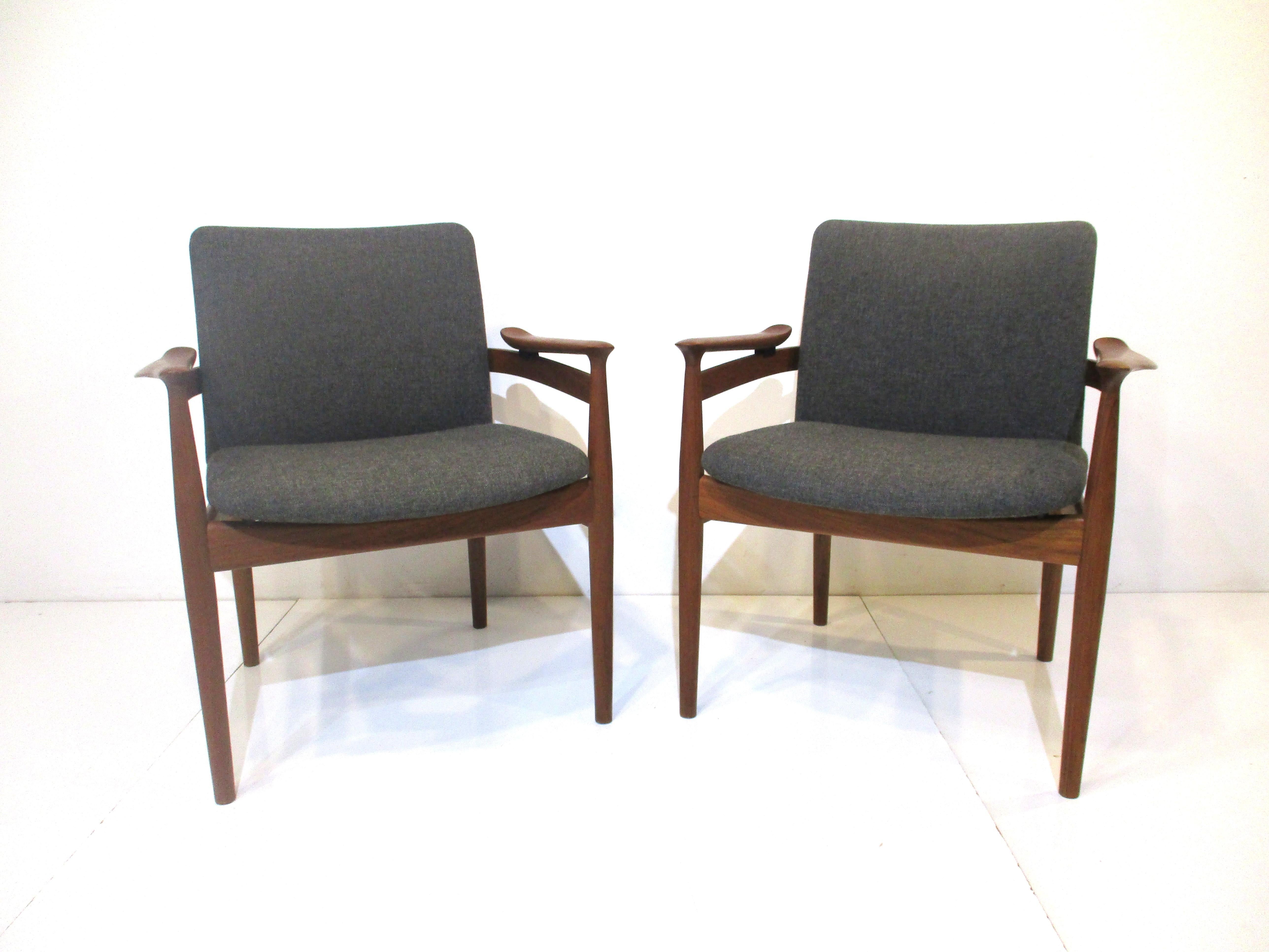 A pair of solid teak arm chairs with original gray tightly woven upholstered seats and wonderfully formed sculptural arms. From the iconic Danish designer Finn Juhl who's works transcended from a long line of skilled cabinet makers and artists who