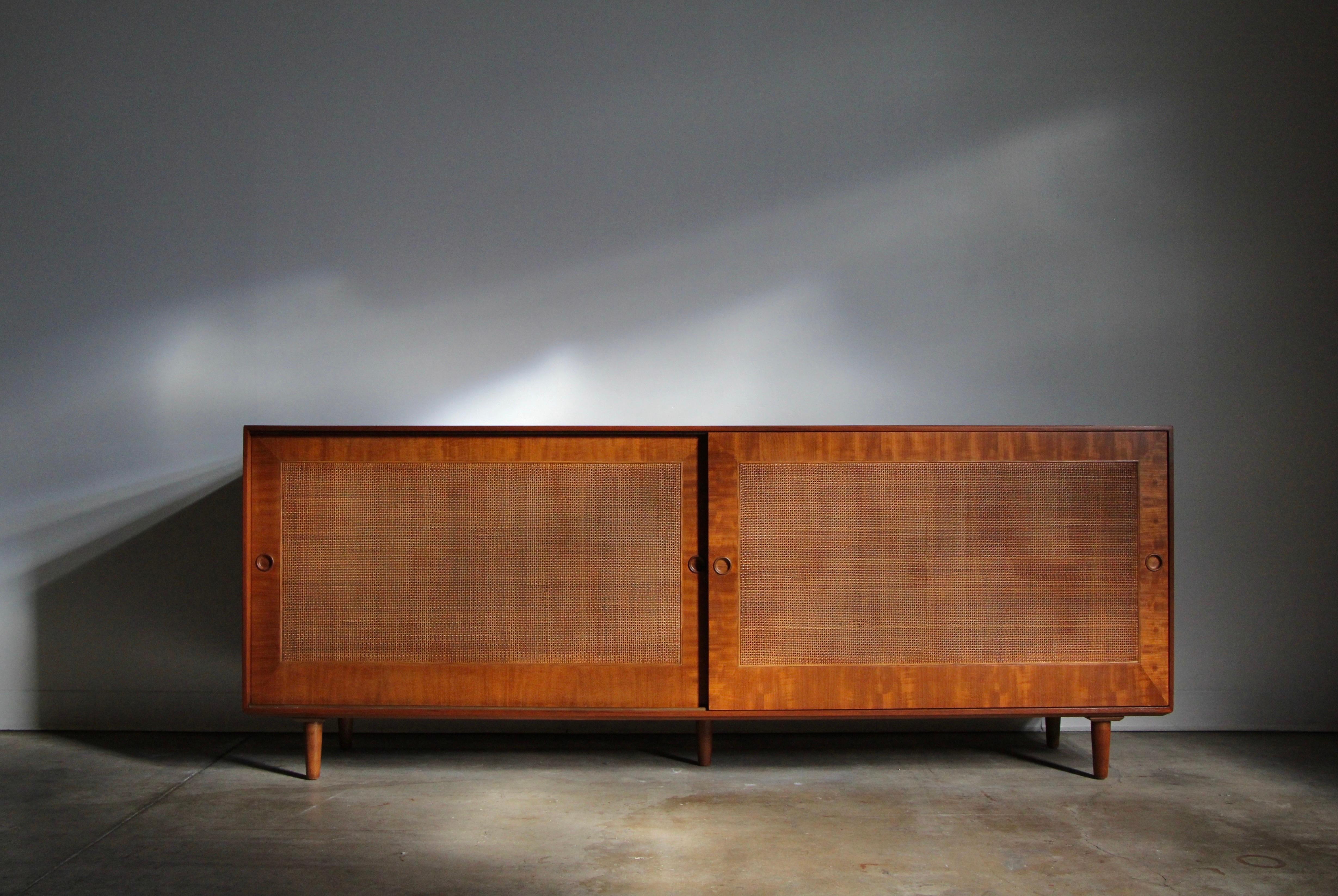 A stunning credenza designed by Finn Juhl for Baker circa 1950’s, constructed in teak wood and natural fiber. This wonderfully understated design is adorned with two sliding cane doors and round recessed pulls that reveal ample storage space within.