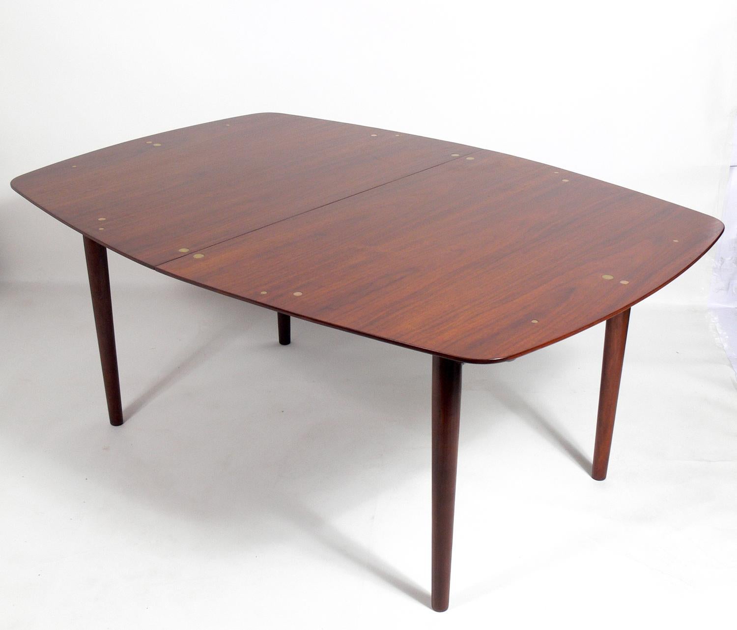Danish modern design dining table, designed by Finn Juhl for baker, circa 1950s. It has been refinished and is ready to use. Constructed of beautifully grained walnut with inset brass medallions, similar to his 
