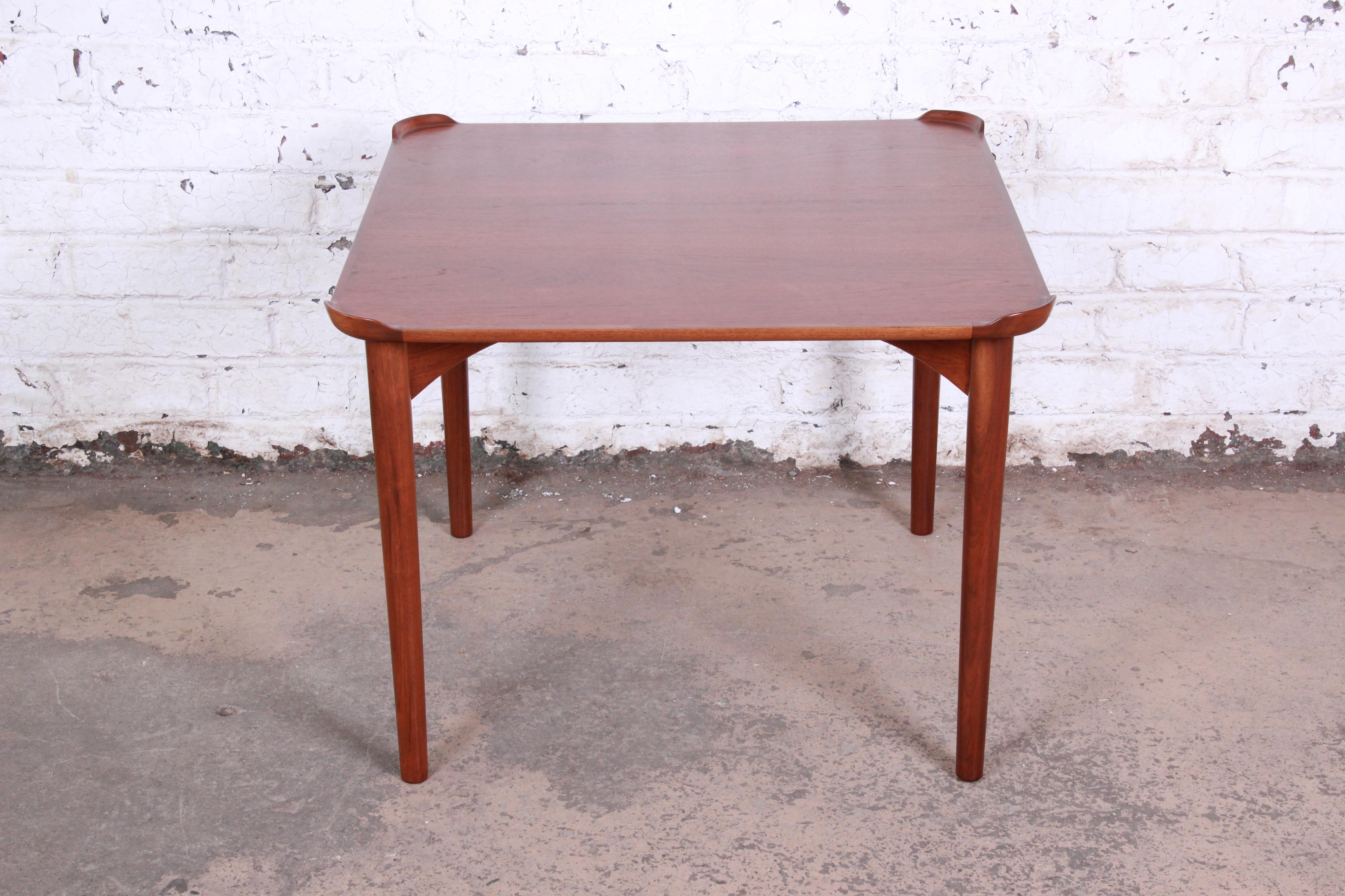 A handsome teak game table designed by Danish architect Finn Juhl for Baker Furniture. The table features stunning teak wood grain and unique carved corner drink backsplashes. Minimalist mid-century Danish Modern design at its finest. The table has