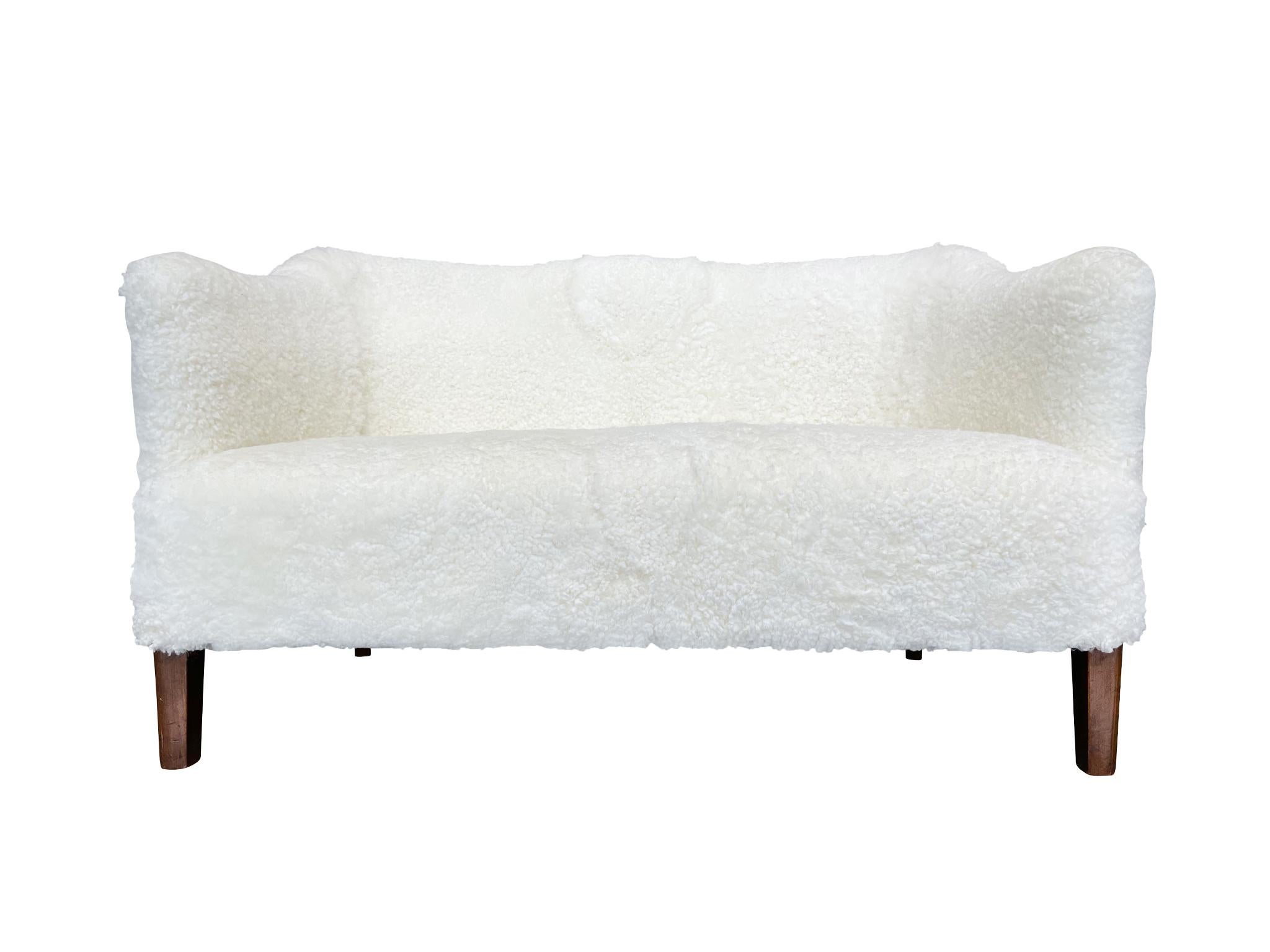 Midcentury Danish settee in the style of Finn Juhl. The settee's design is one of soft curves and rounded edges. The back curves subtly inward at the middle, creating an elegant furrow. Newly reupholstered in a white shearling from Skandilock, this