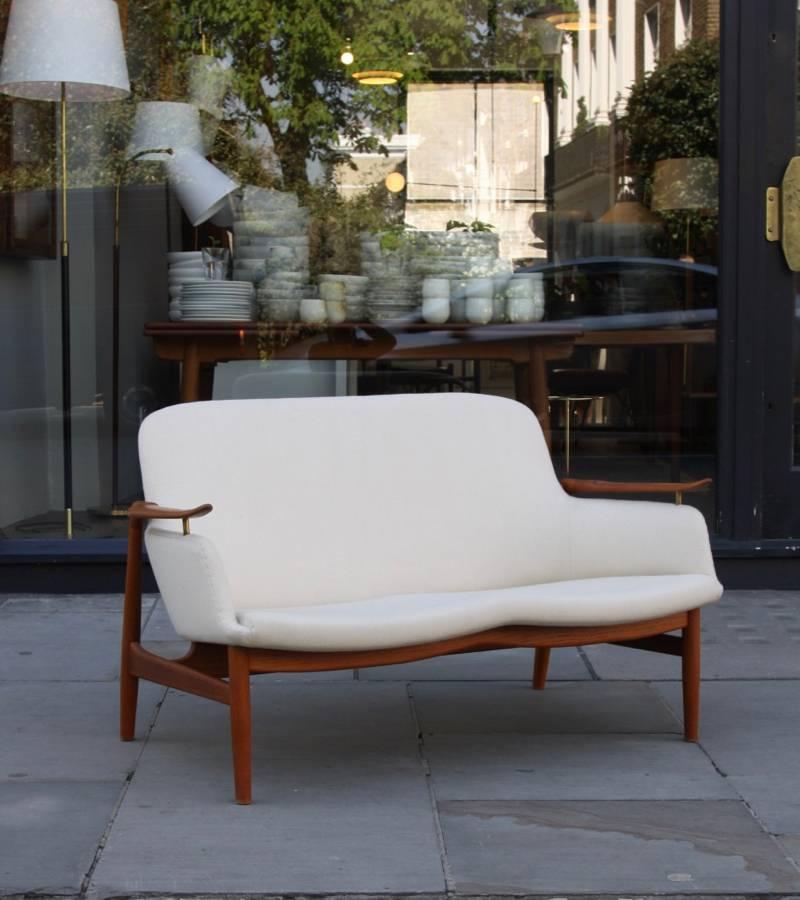 NV53 two-seat sofa designed by Finn Juhland made by master cabinetmaker Niels Vodder, Denmark, 1950s. The frame is carved out of teak and covered in a creamy white cotton upholstery. The sculptural arms pointing up and forward, the carefully