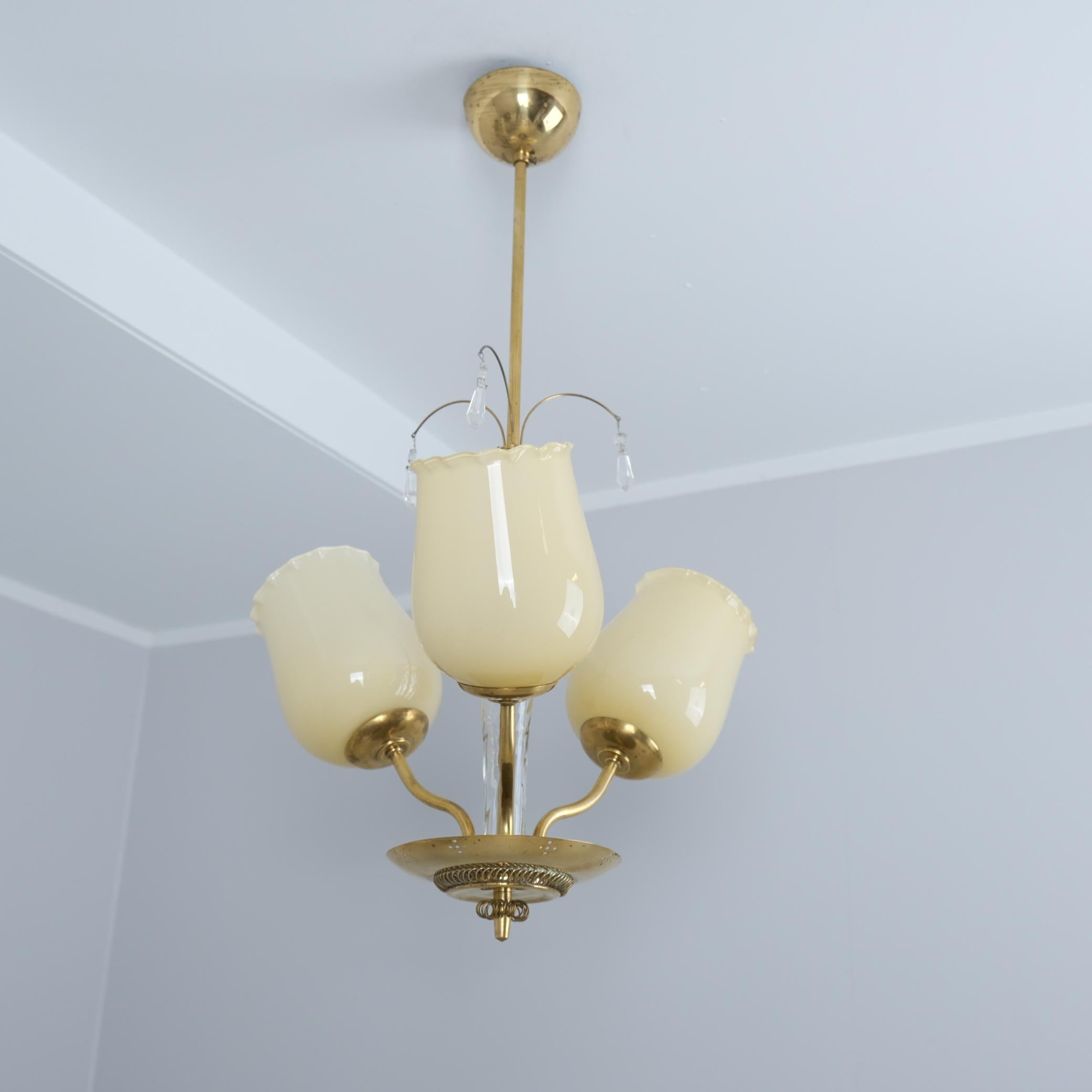 Pendente da soffitto finlandese Mid-Century Modern modello 62-004/3 dal catalogo Stockmann. La lampada presenta un corpo in ottone con una ciotola decorata e perforata con decorazioni in cristallo e vetro. Il modello ha tre lampadine dietro a