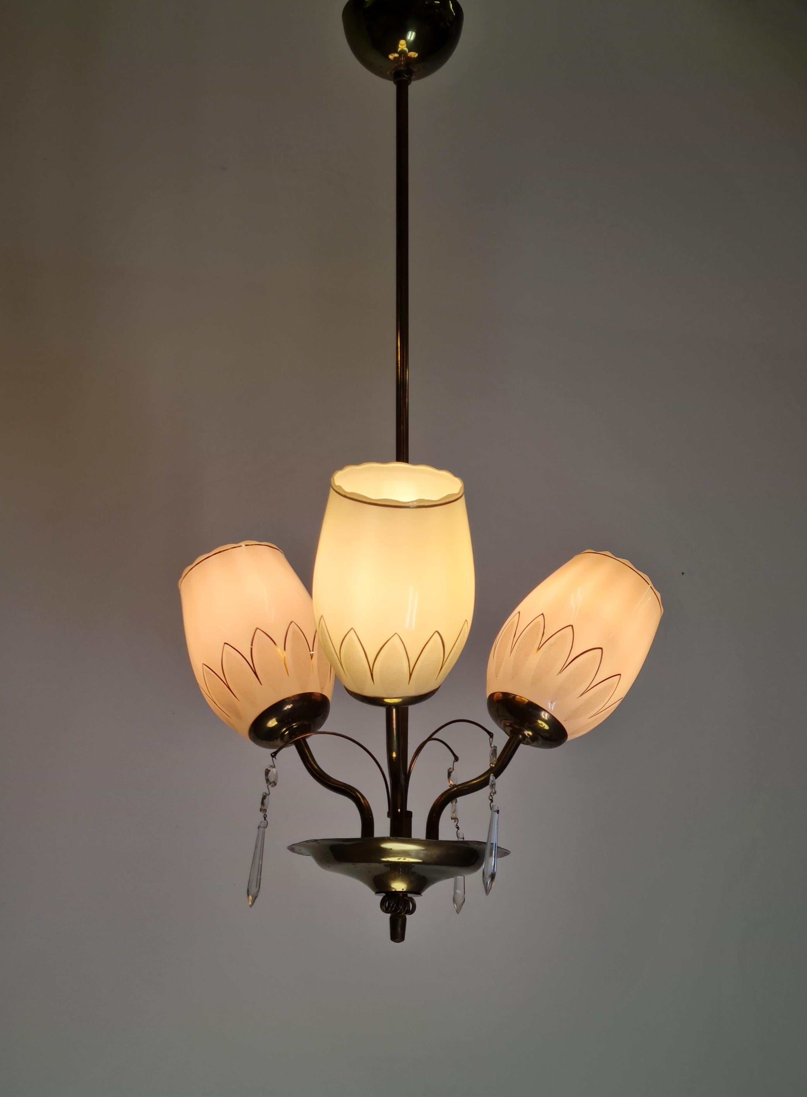 Pendente da soffitto finlandese Mid-Century Modern modello 62-402/3 dal catalogo Stockmann. La lampada presenta un corpo in ottone con una ciotola decorata e perforata con decorazioni in cristallo e vetro. Il modello ha tre lampadine dietro a