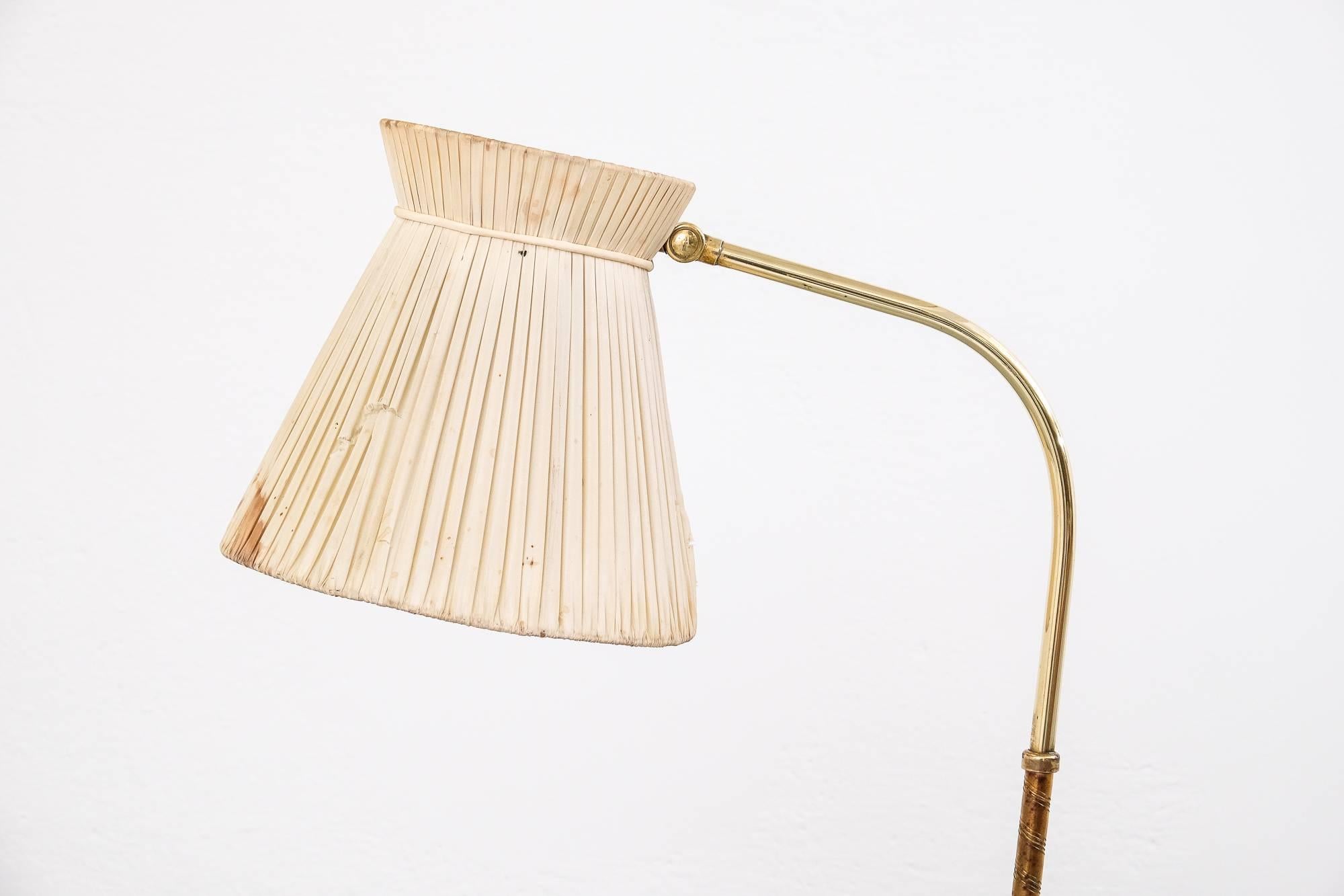 A Lisa Johansson-Pape model 2063 floor lamp for Orno Oy, Finland. The lamp has a curved brass frame, partially wrapped in plastic ribbon. It has an adjustable hood with an original pleated fabric shade and a plexiglass diffuser on top. Marked by