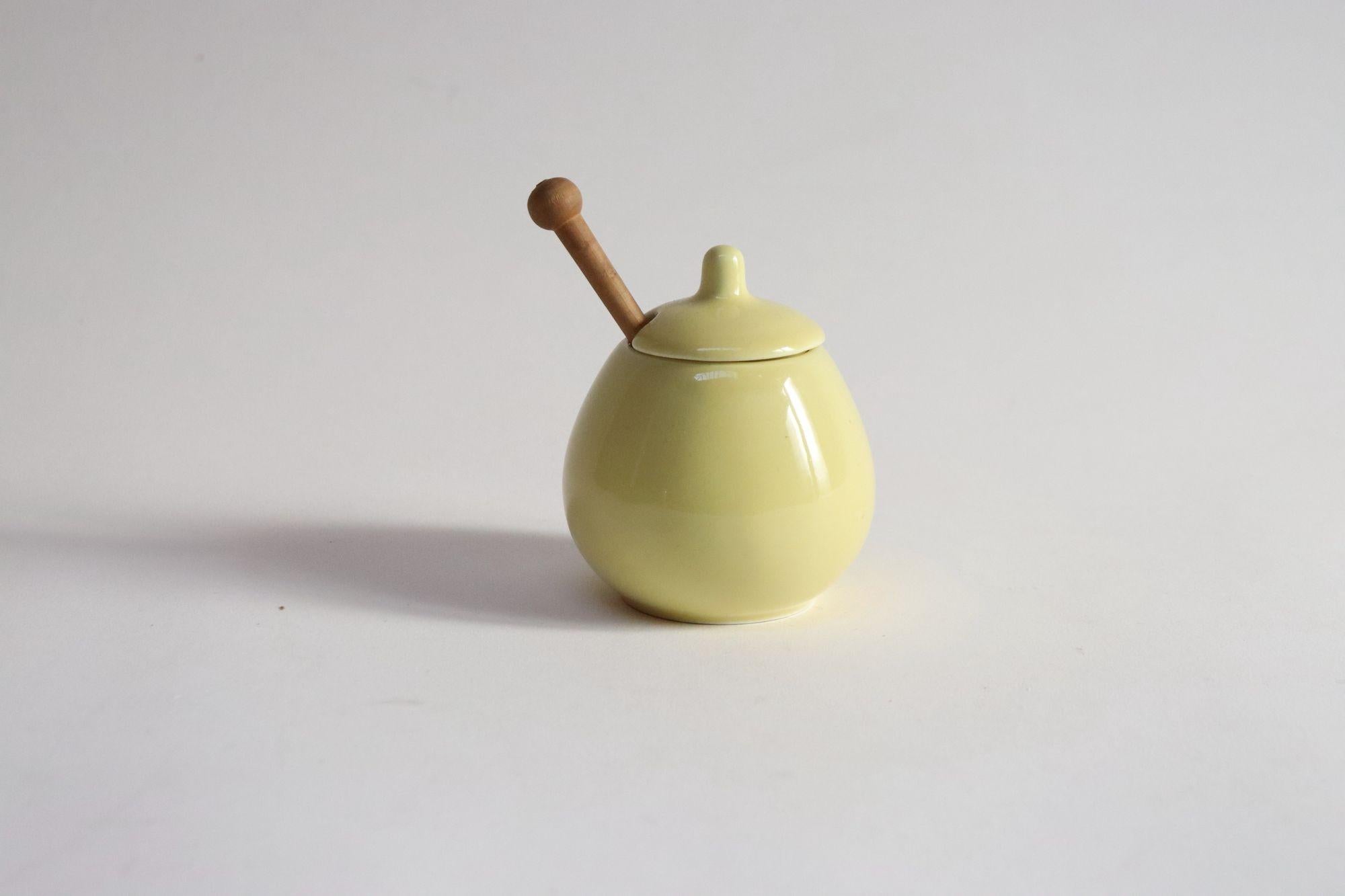 Petite jarre à épices/miel/moutarde jaune pâle avec cuillère en bois originale conçue par Kaj Franck pour Arabia dans le cadre de la série Kilta produite entre 1953-1974 (ca. 1964, Finlande).
Charmant et coloré, il s'intègre à toutes les
