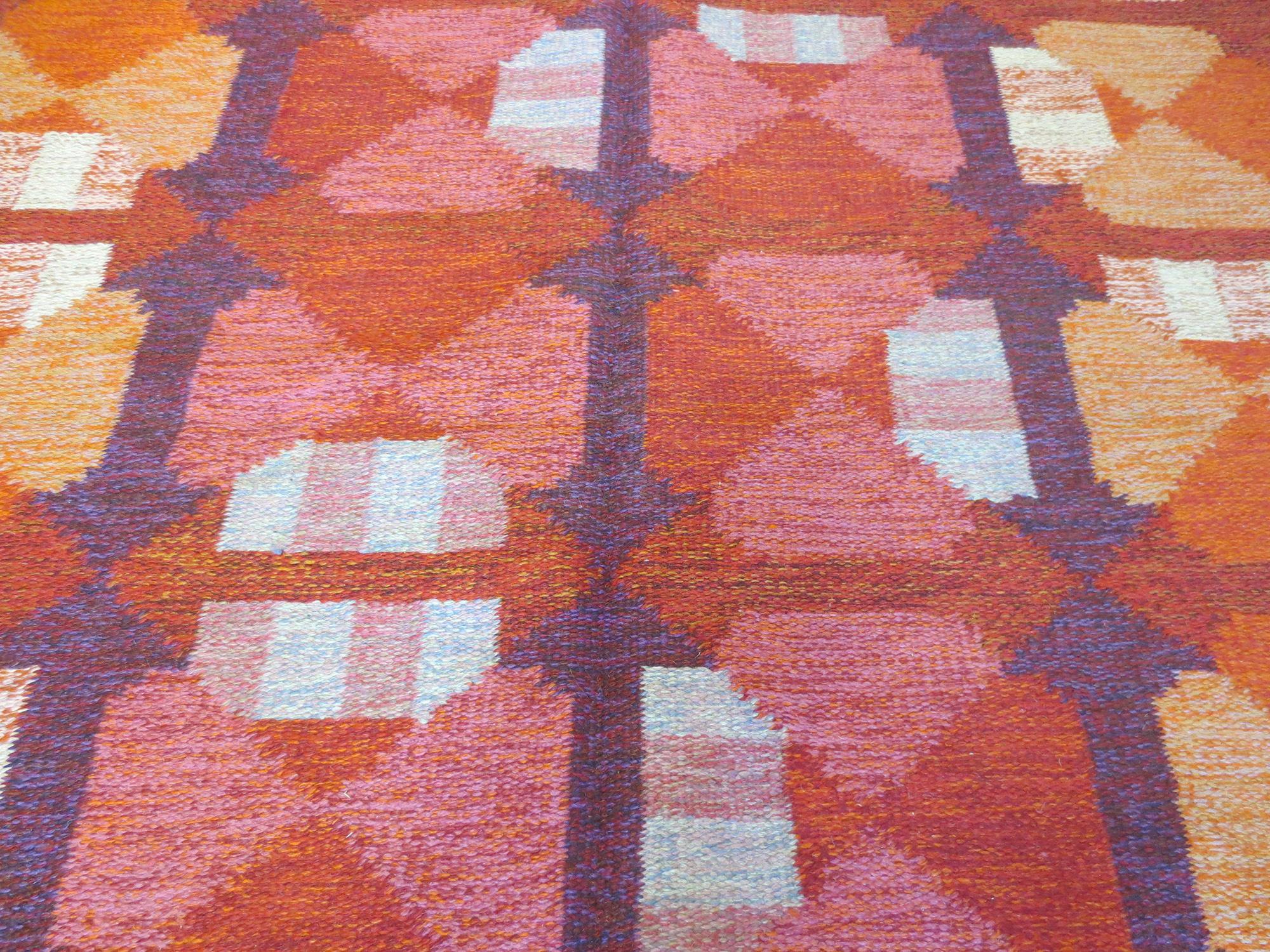 This is a Finnish vintage rug signed by textile artist, Alestasalon Mottokutomo, from the mid-20th century and in excellent condition. It is handwoven with shades of bold and vivid reds, oranges, pinks, and purples in a beautiful abstract geometric