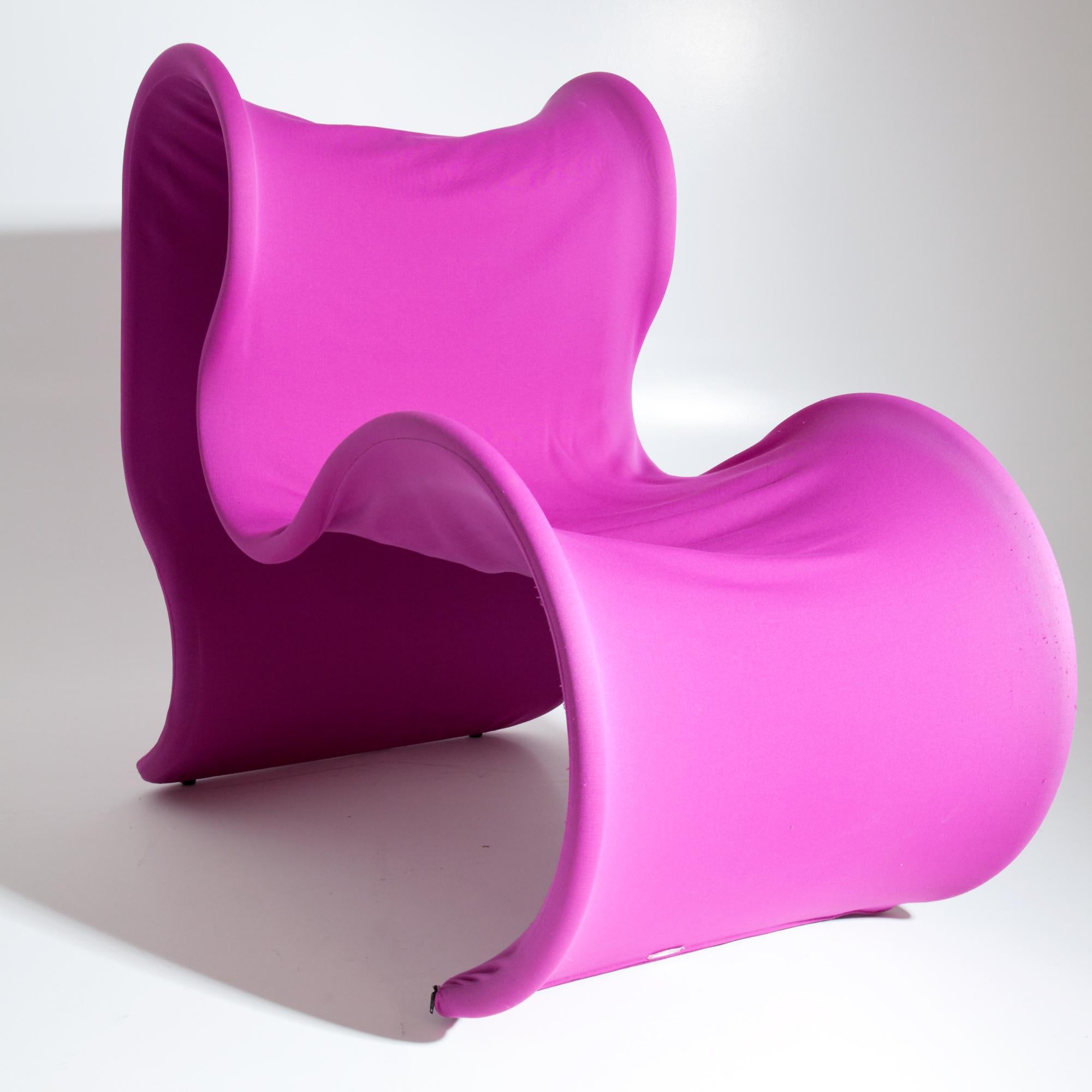 Curved armchair with pink fabric cover placed over steel tube stretched. Small plaque 