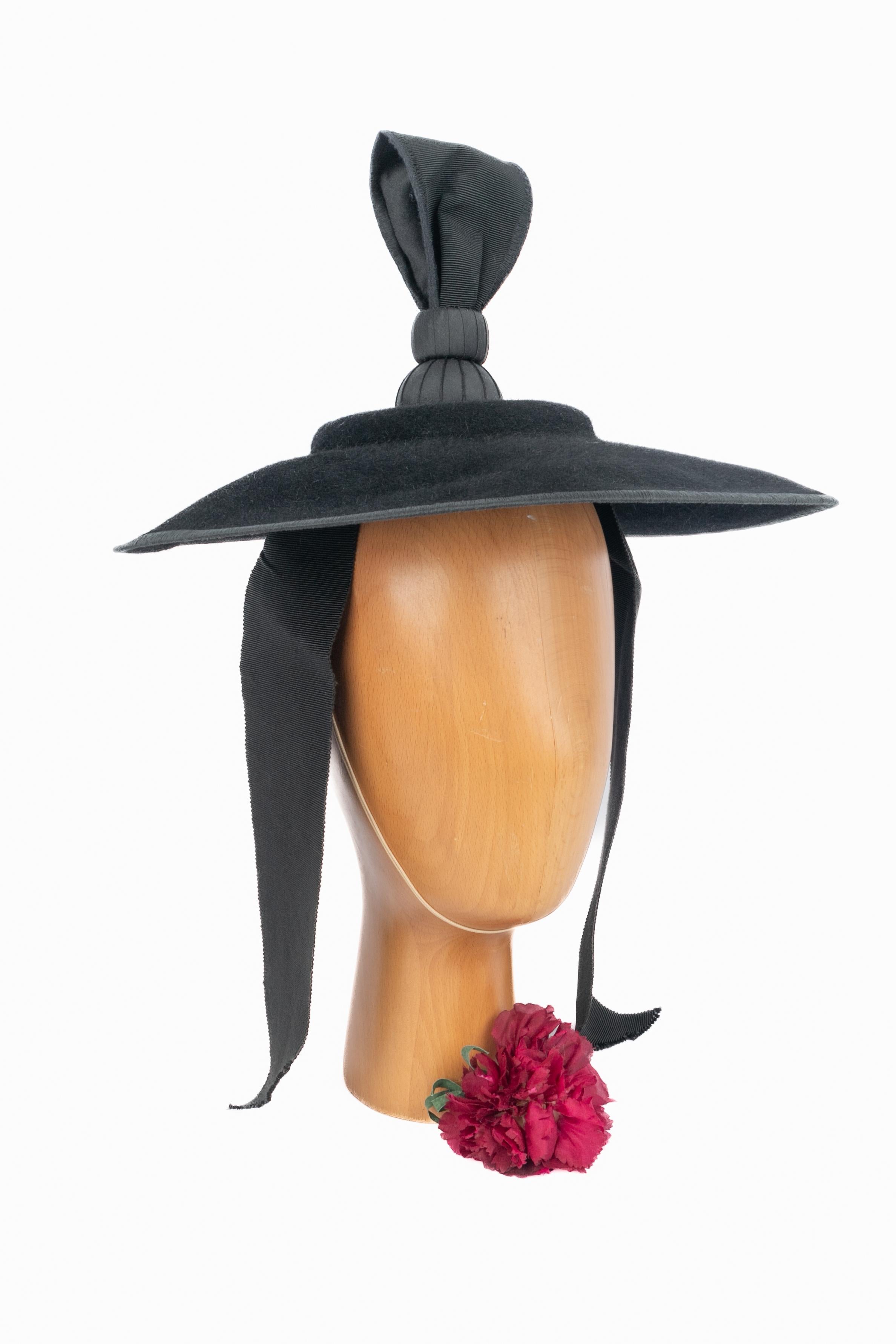 FIONA BENNETT - Chapeau plat en moleskine noire en forme de lapin surmonté d'une décoration en ruban de grain et d'une fermeture à deux rubans.

Condit :
Très bon état.

Dimensions :
Diamètre : 36 cm

SKU:CHP193