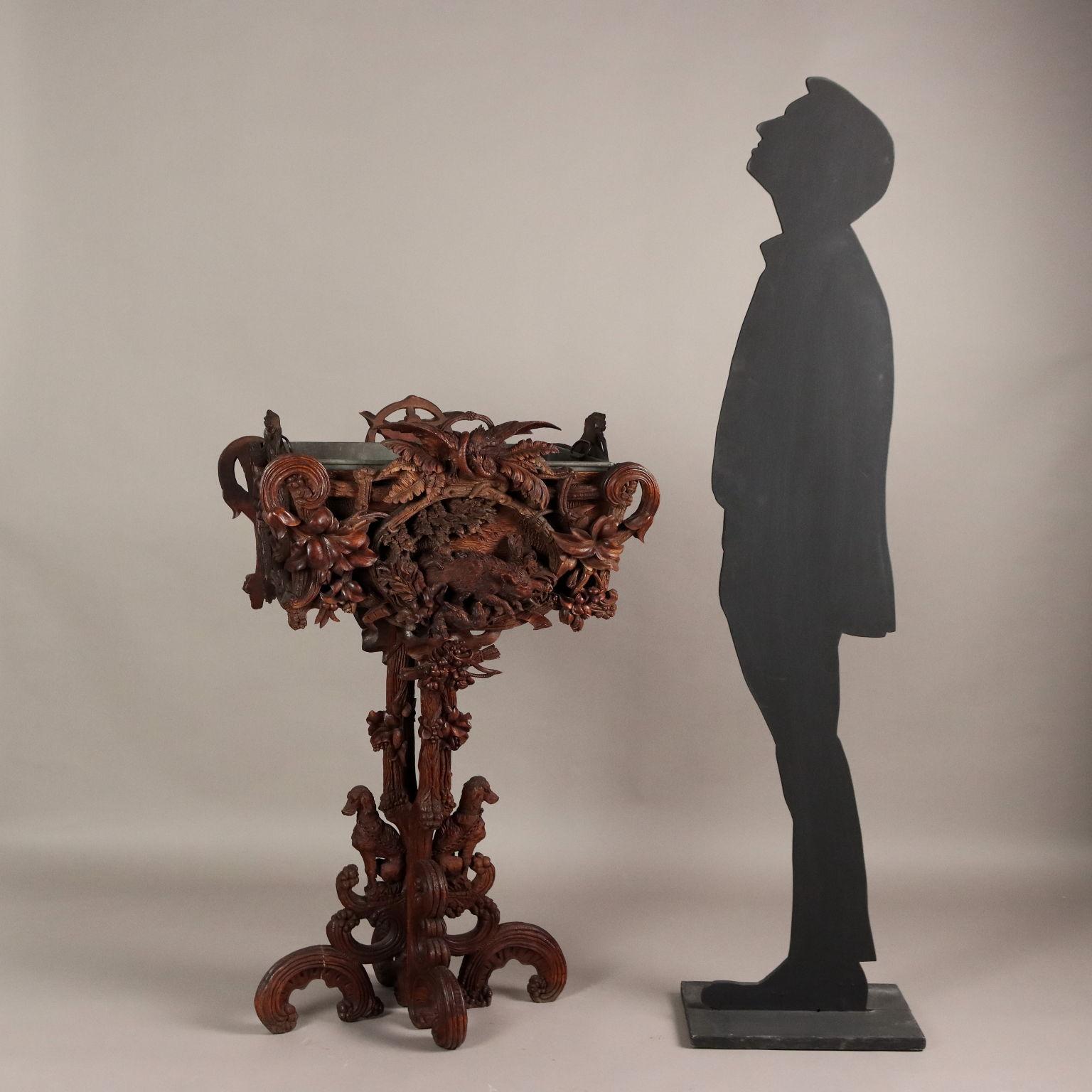 Black Forest planter from the late 19th century. Made of richly carved walnut wood. The four feet, like the supporting shaft, are carved in the guise of twisted branches on which ivy branches are twisted, resting on two feet are two carved dogs.