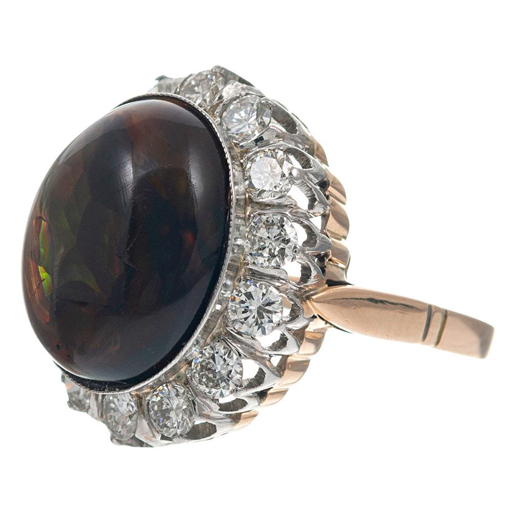 A cabochon of fire agate exhibits impressive liveliness from its classic setting, with white diamonds creating its scalloped border. The major stone measures 14.3 x 12.0 millimeters. This gem is unusual and beautiful- with excellent play of color