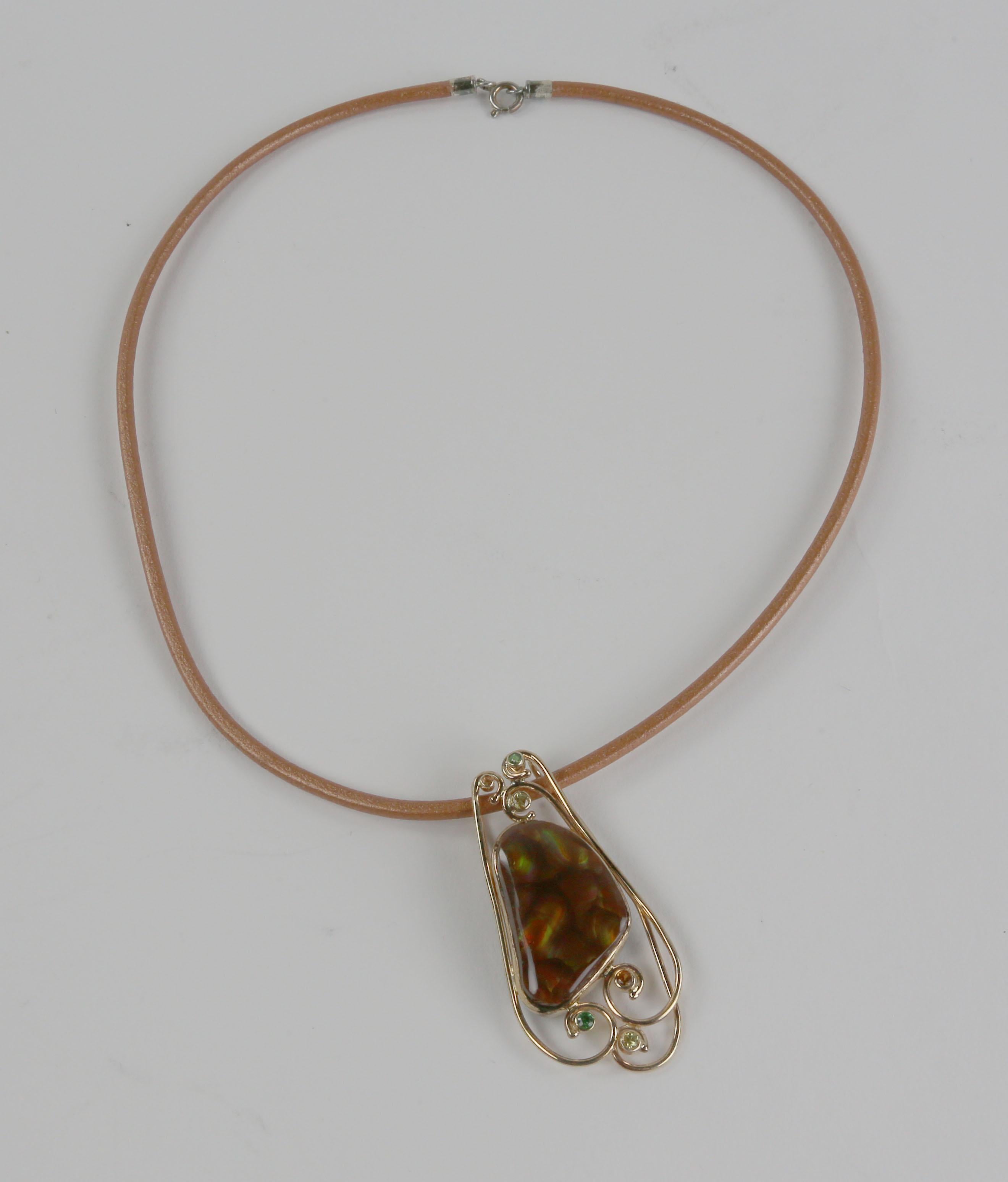 Ce collier pendentif élégant et subtil est composé d'une magnifique pierre d'agate de feu, rehaussée de saphir et de tsavorite, le tout monté dans une monture en or jaune 18 carats fabriquée à la main. La plaque arrière en argent sterling fabriquée