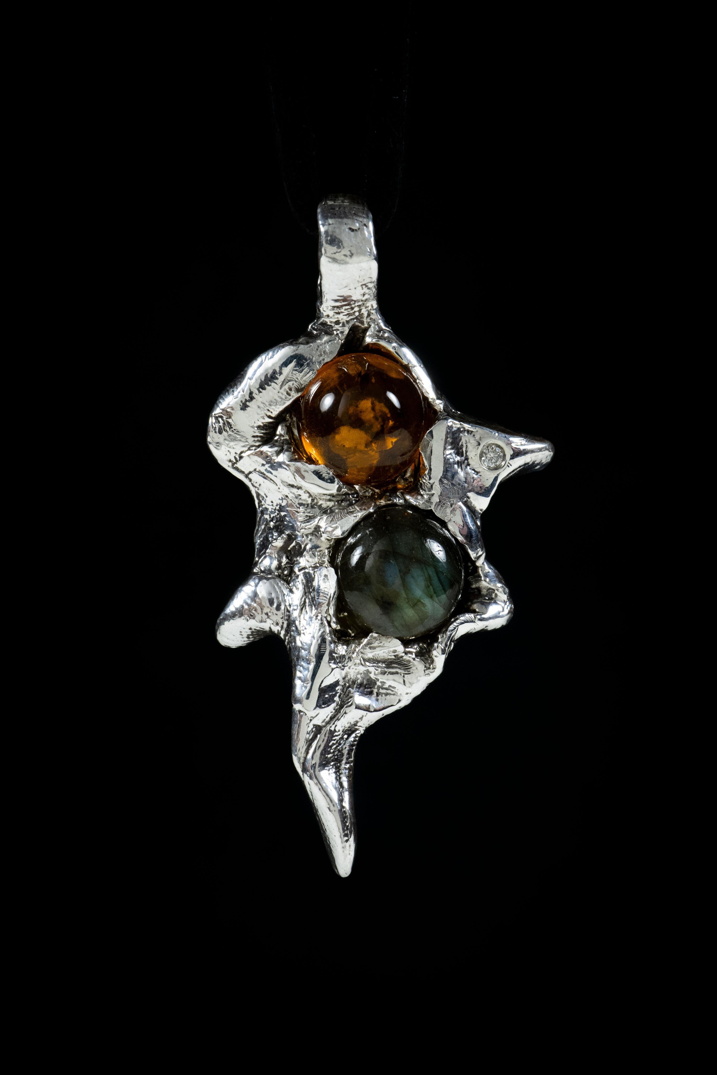 Fire and Water is a one-of-a-kind pendant by Ken Fury that is hand-carved and cast in sterling silver with amber, labradorite, and genuine diamond.

Metal: Sterling Silver

Stones: Amber, Labradorite, and Genuine Diamond.

Size: 32mm x