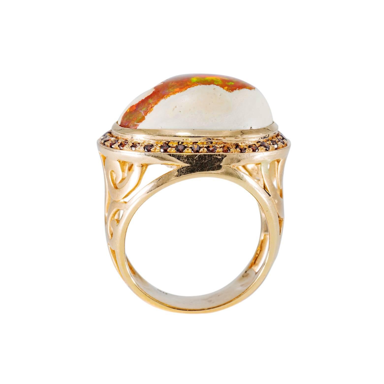 This stunning fire opal is beautifully surrounded by burnt orange diamonds. The base of the ring is intricately carved  and even though it is a hefty ring it is surprisingly comfortable. The opal is aprox. 10 1/2 carats  and the ring is a size 8.