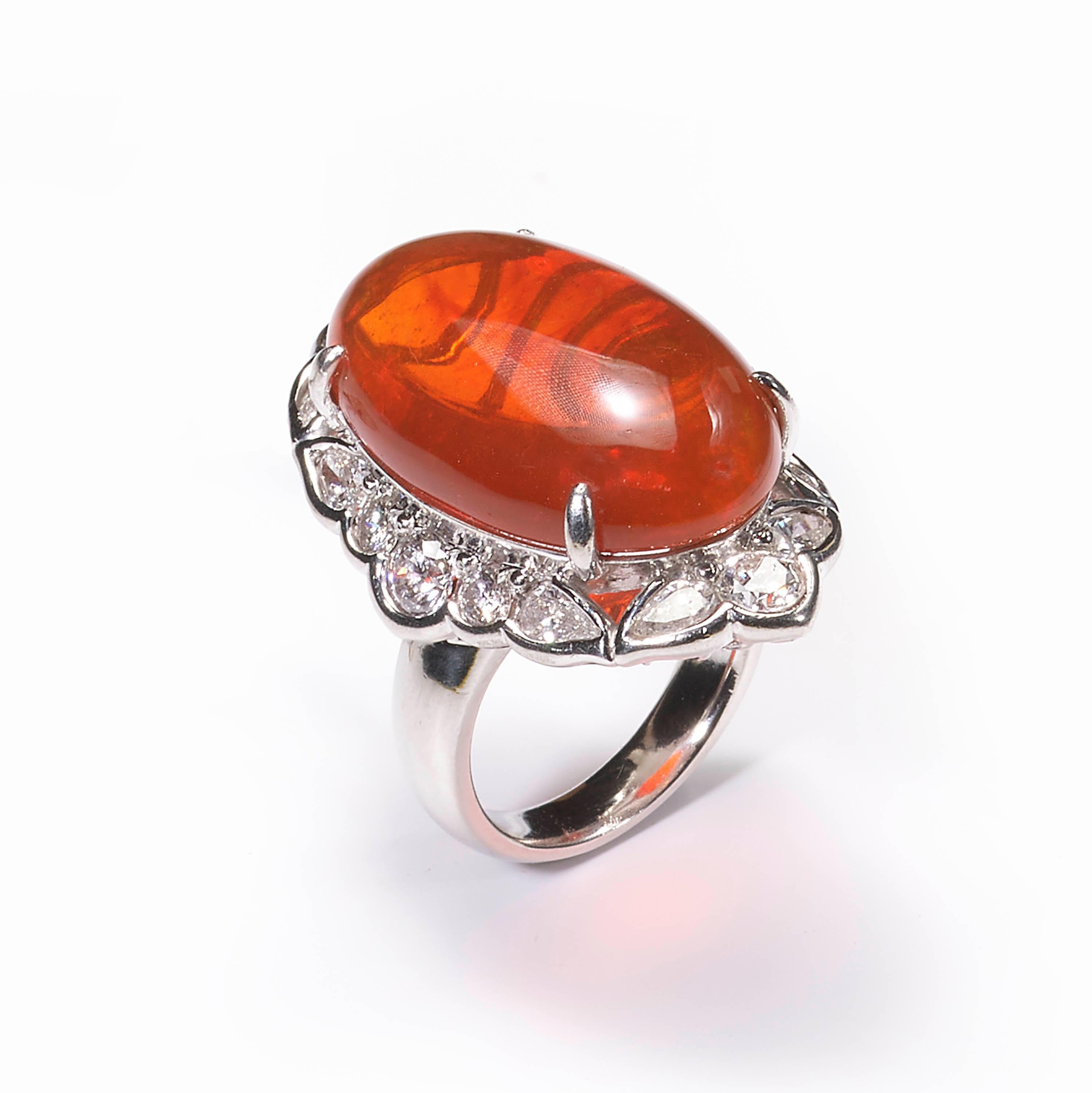A modern fancy cluster ring, set with a central oval shaped cabochon-cut fire opal, weighing an estimated 18.00 carats, surrounded by alternating round brilliant-cut diamonds and pear-cut diamonds, weighing an estimated total of 2.40 carats, all