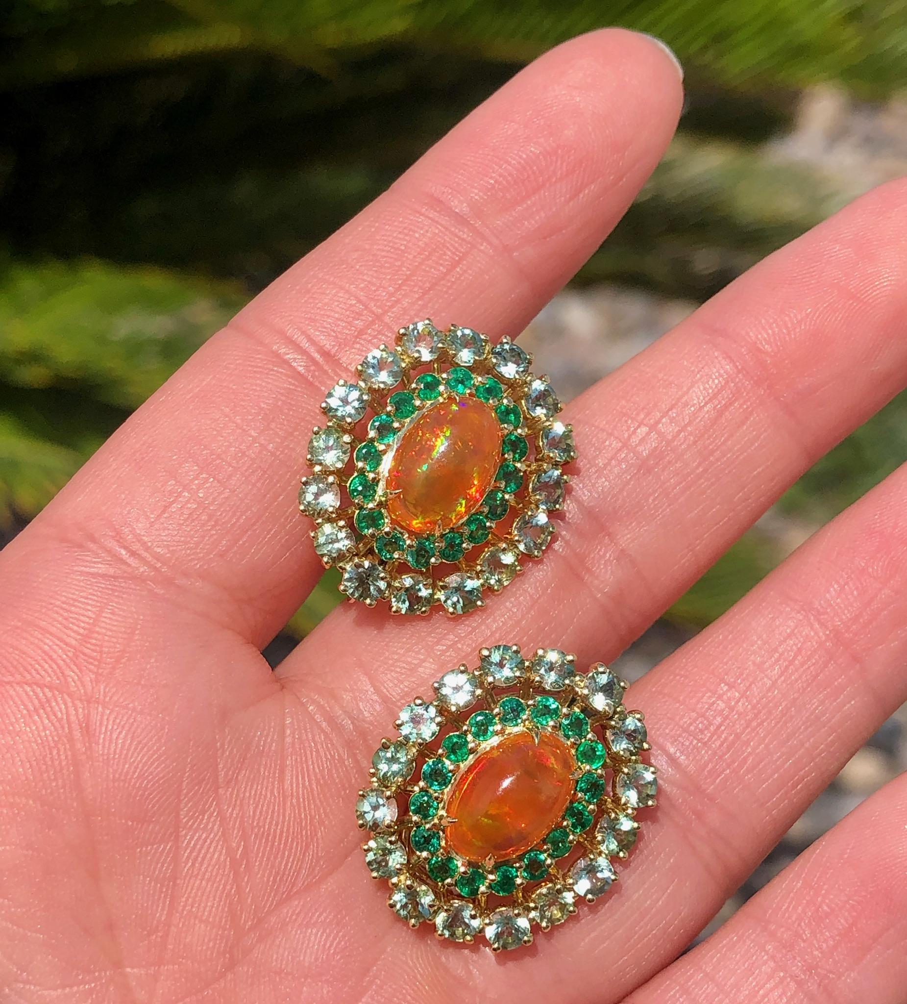 Very Fine 4.31 ctw Cabochon Mexican Fire Opals with amazing play-of-color. The exquisite stones are surrounded by 1.28 carats of round Colombian emeralds and 3.84 carats of Green Tourmalines and set in 18K Yellow Gold. The color combinations