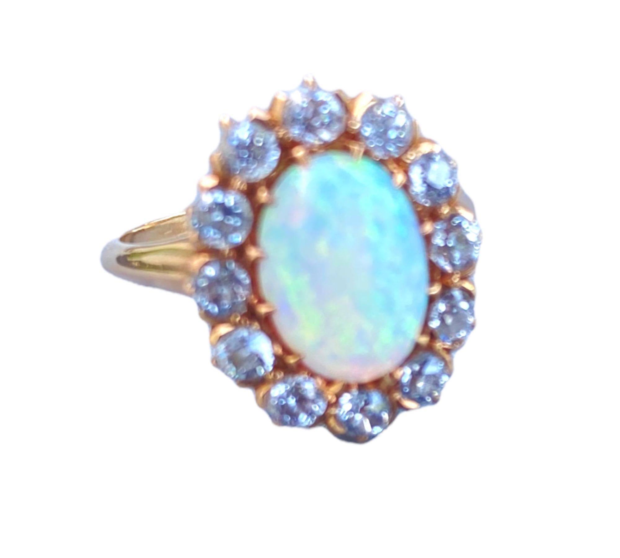 12 European Cut diamonds surround a fiery oval-shaped opal. The ring measures 13  x 16 mm in diameter and is made of 14 karat gold. The metal is yellow with a pinkish tint of color. Great contrast to showcase this gorgeous Opal. 
The European cut