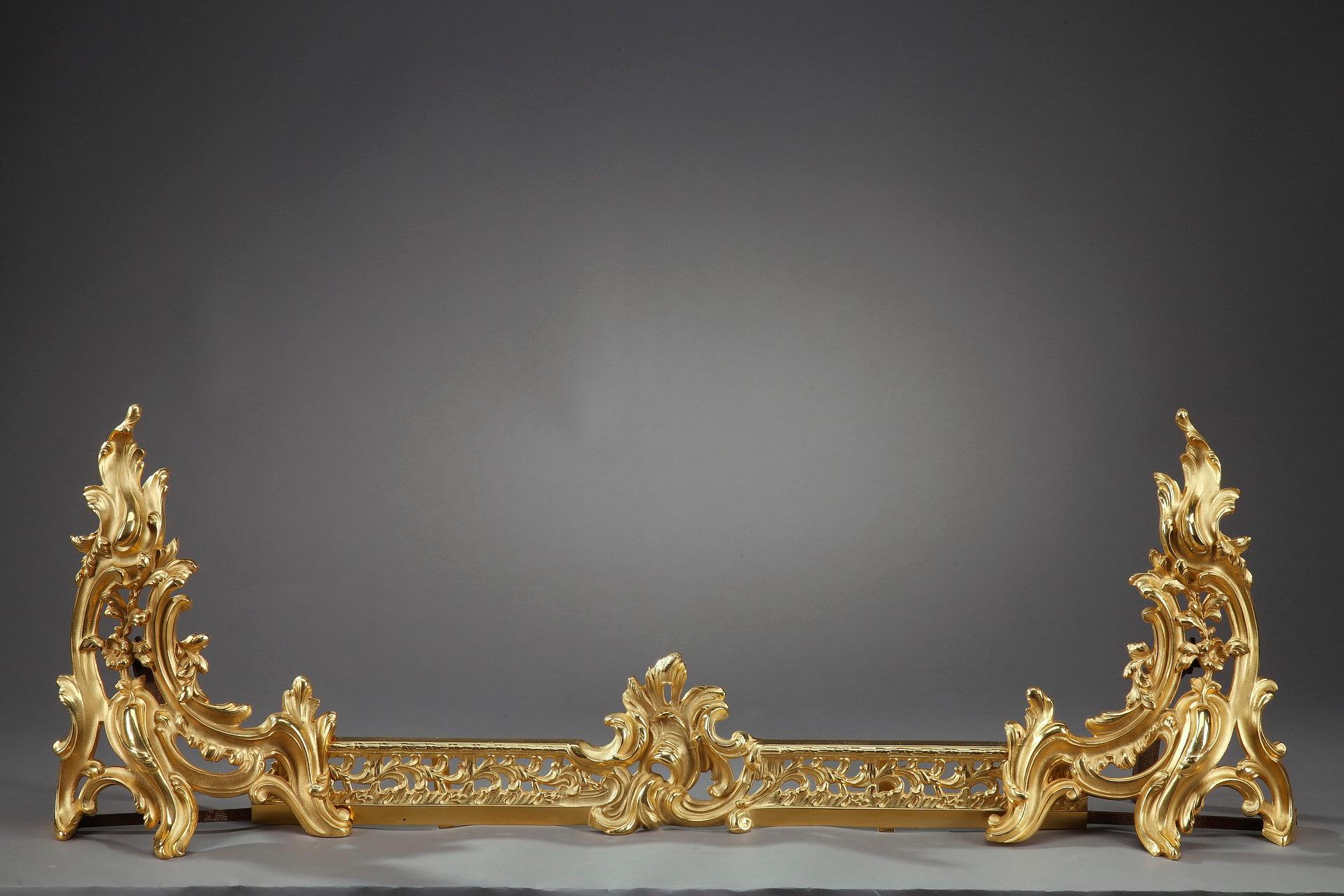 Fire screen crafted of gilt and chiseled bronze featuring an intricate decoration of scrolls, acanthus leaves and flowers in Rococo style. With a fireplace fender and a pair of andirons, or chenets, embellished with naturalistic motifs in Louis XV