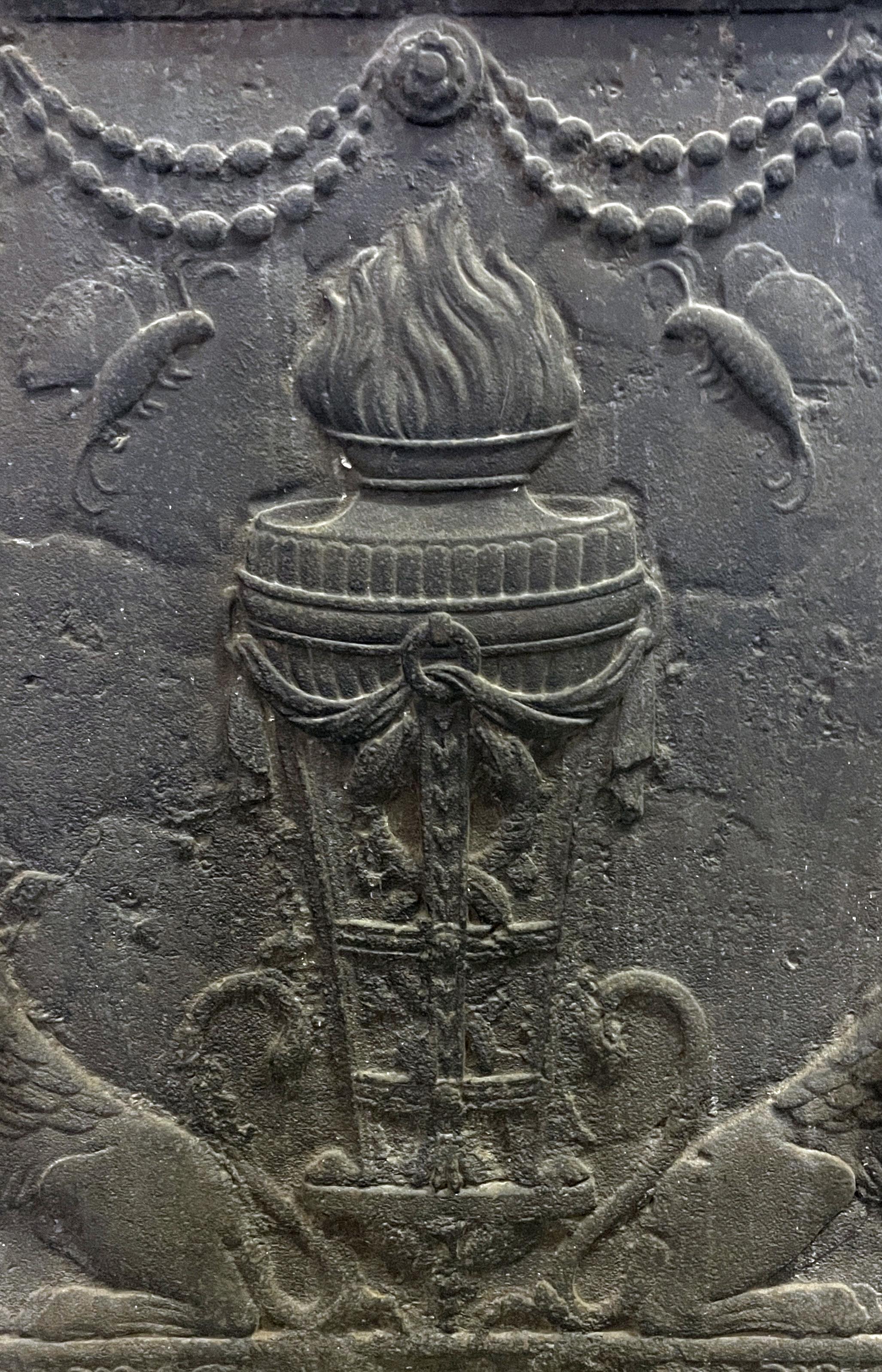 Kaminboden aus dem 19. Jahrhundert, der eine Vase auf einem Dreibein mit Feuer darstellt, eingerahmt von zwei Chimären, die Körbe mit Früchten tragen.