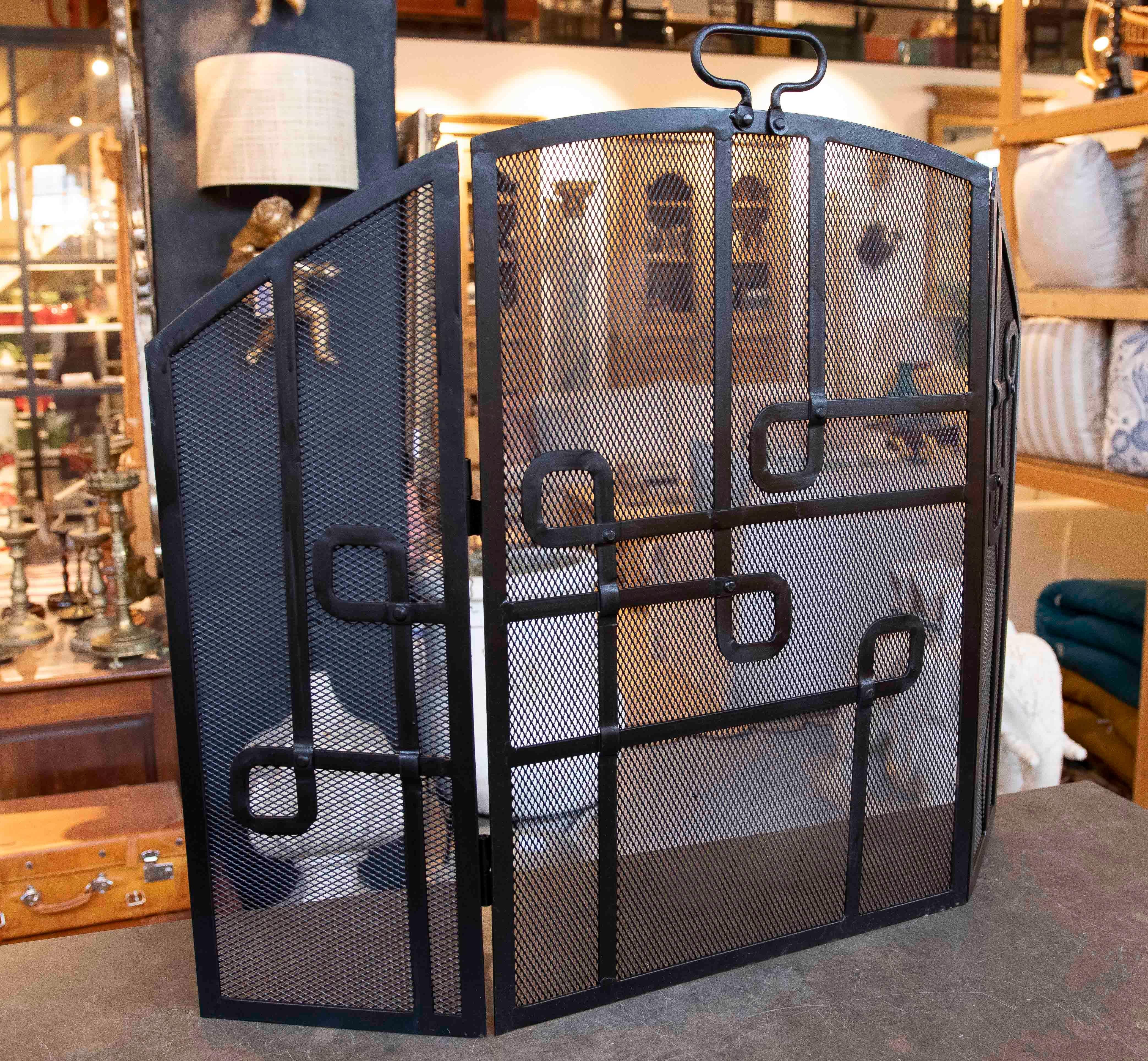 Kaminschirm aus schwarzem Eisen mit einer widerstandsfähigen Struktur und einem feinmaschigen Metallgitter für mehr Sicherheit. Sein Design umfasst geometrische Details in Form von ineinandergreifenden Rechtecken, die einen modernen und funktionalen