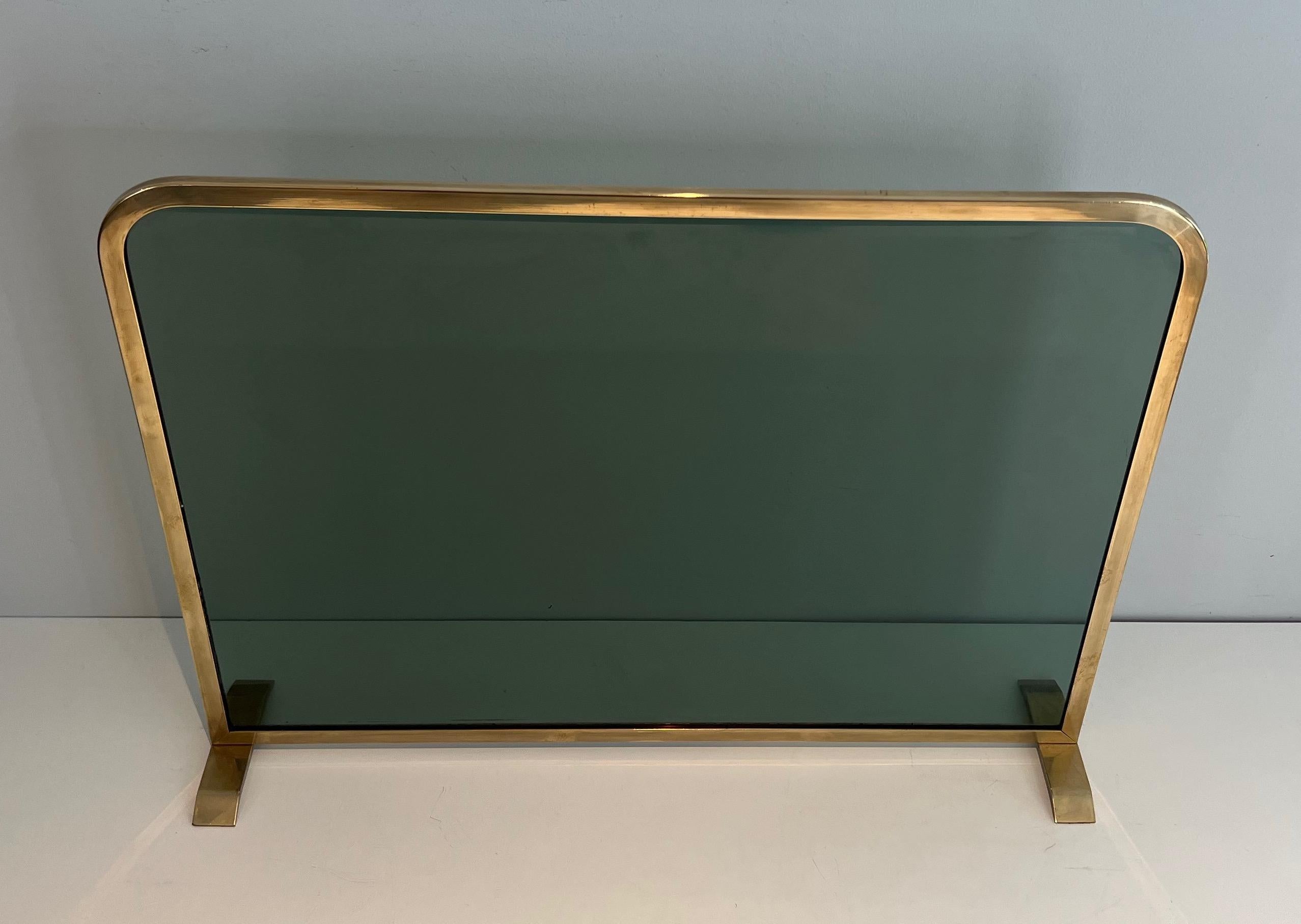 This very nice and elegant fireplace screen is made of a greenish glass panel surrounded by a brass frame. This is a French work. Circa 1970