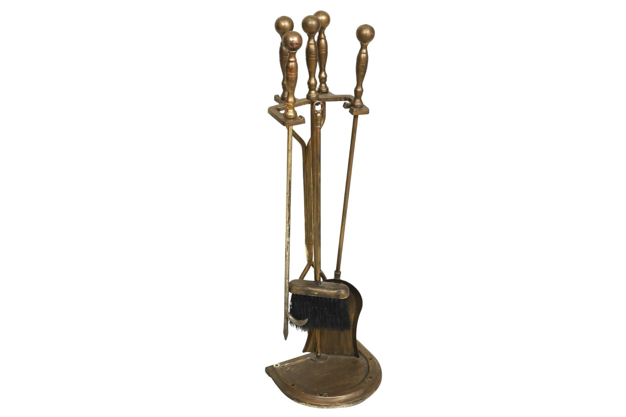 A set of metal fireplace tools with stand. Includes tongs, poker, shovel and brush, each with a contoured beveled handle with ball finial top. Tools hang from a metal yoke with a demilune base.